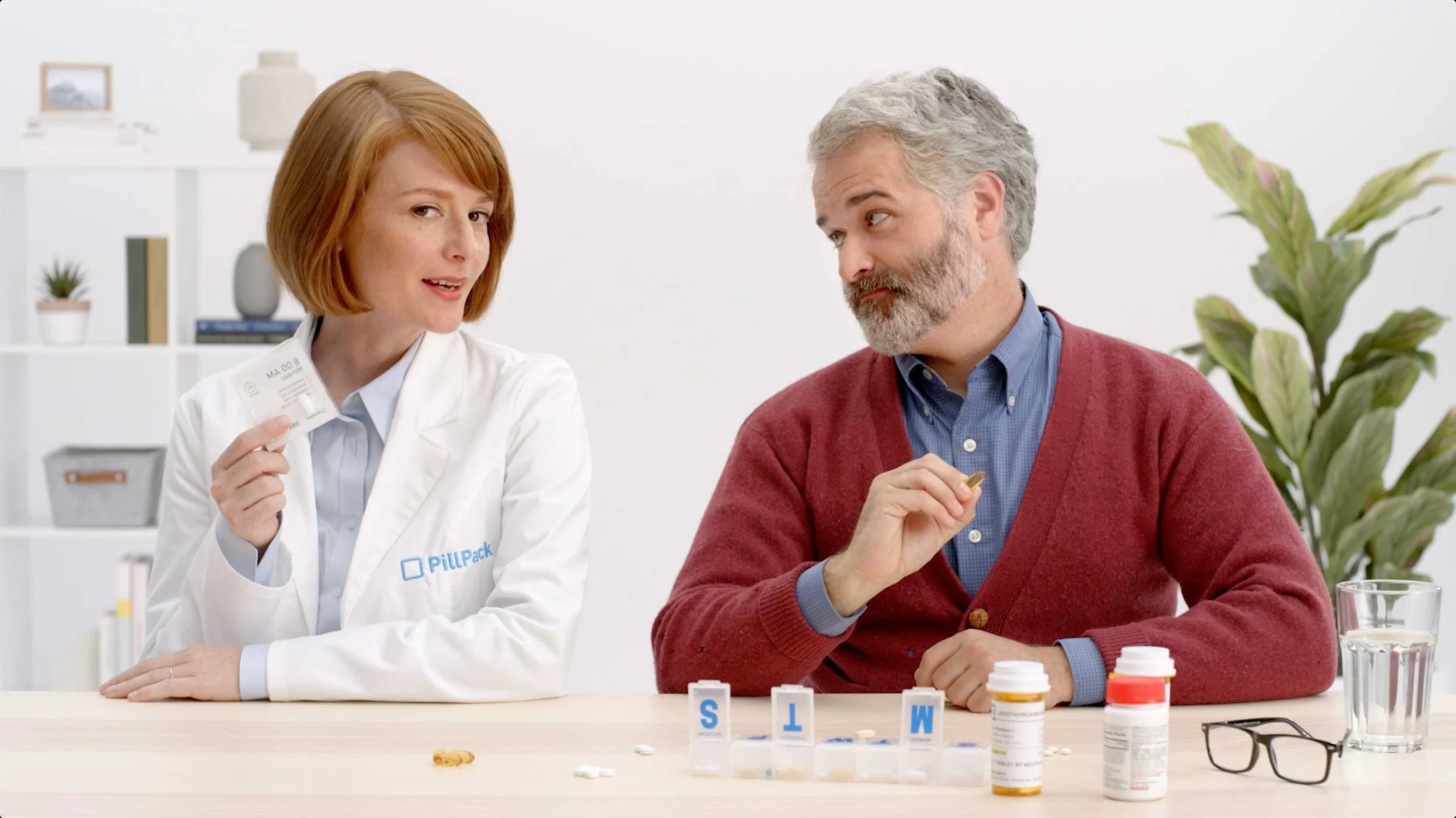 A man and woman sit at a table in a white studio environment in a PillPack explainer video