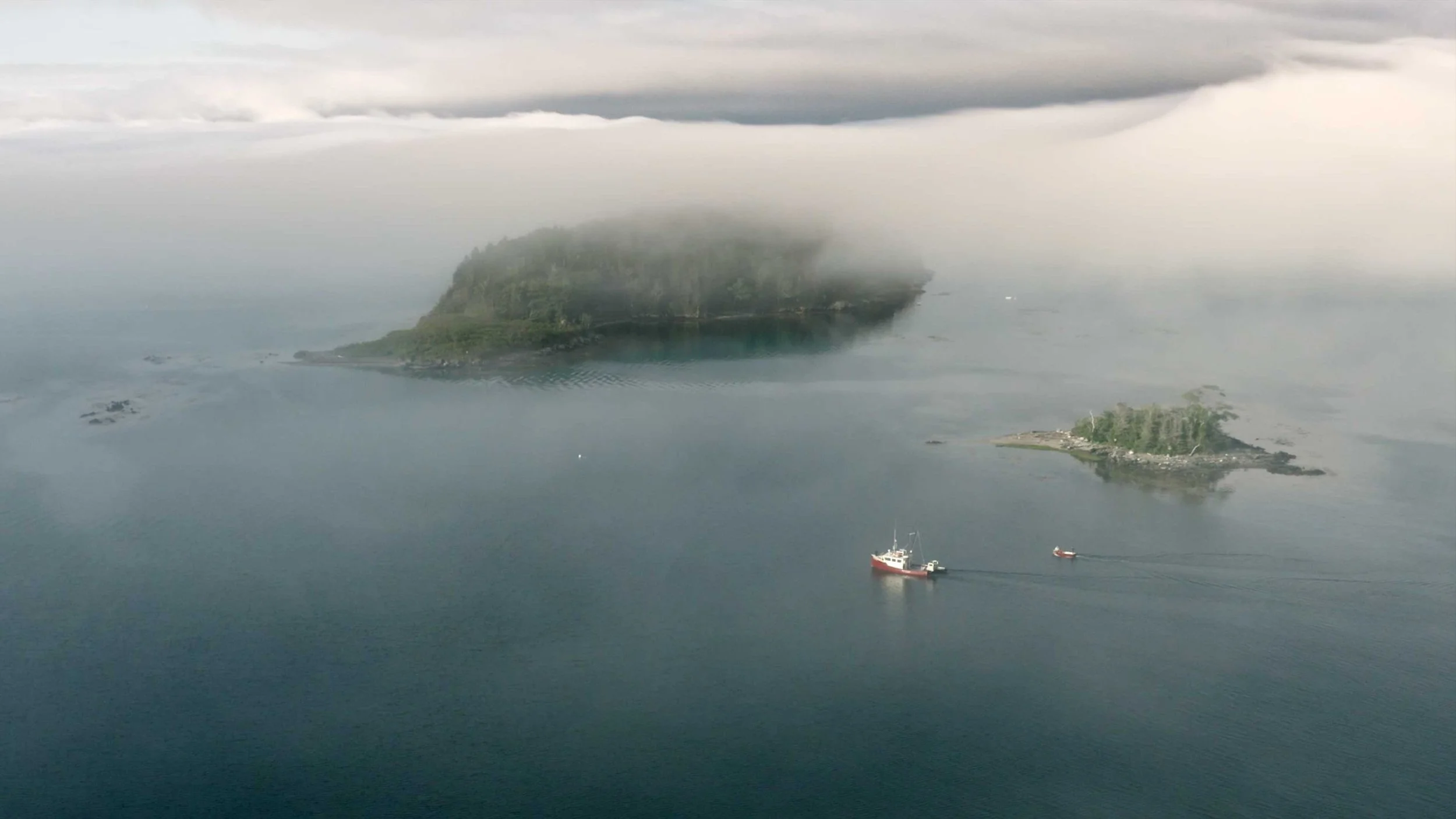 An aerial view of a fishing boat alongside several islands in the morning fog