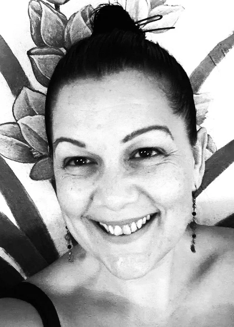 Close-up black and white photo of a smiling woman with her hair in a bun, wearing earrings, with a floral background.