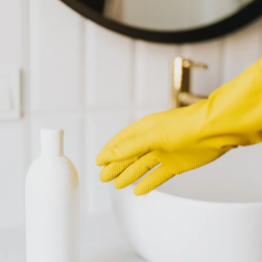 Close-up of a hand wearing a yellow rubber glove, reaching for a white bottle on a kitchen counter.