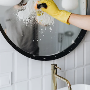 Person cleaning a mirror with a yellow sponge and wearing a yellow glove.
