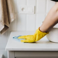 Person wearing yellow rubber gloves cleaning a kitchen countertop with a cloth.