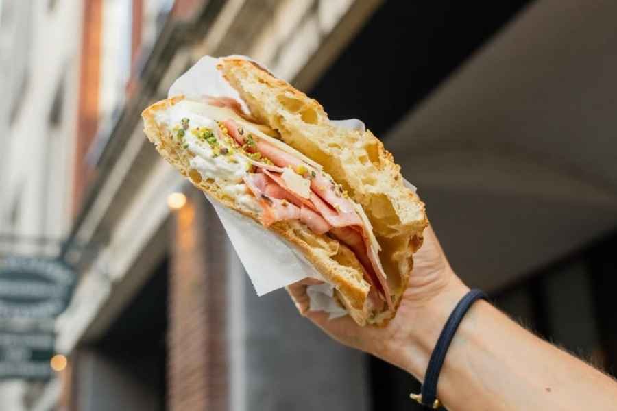 Hand holding a half-eaten sandwich with bread, turkey, mayonnaise, and shredded lettuce, wrapped in white paper outside