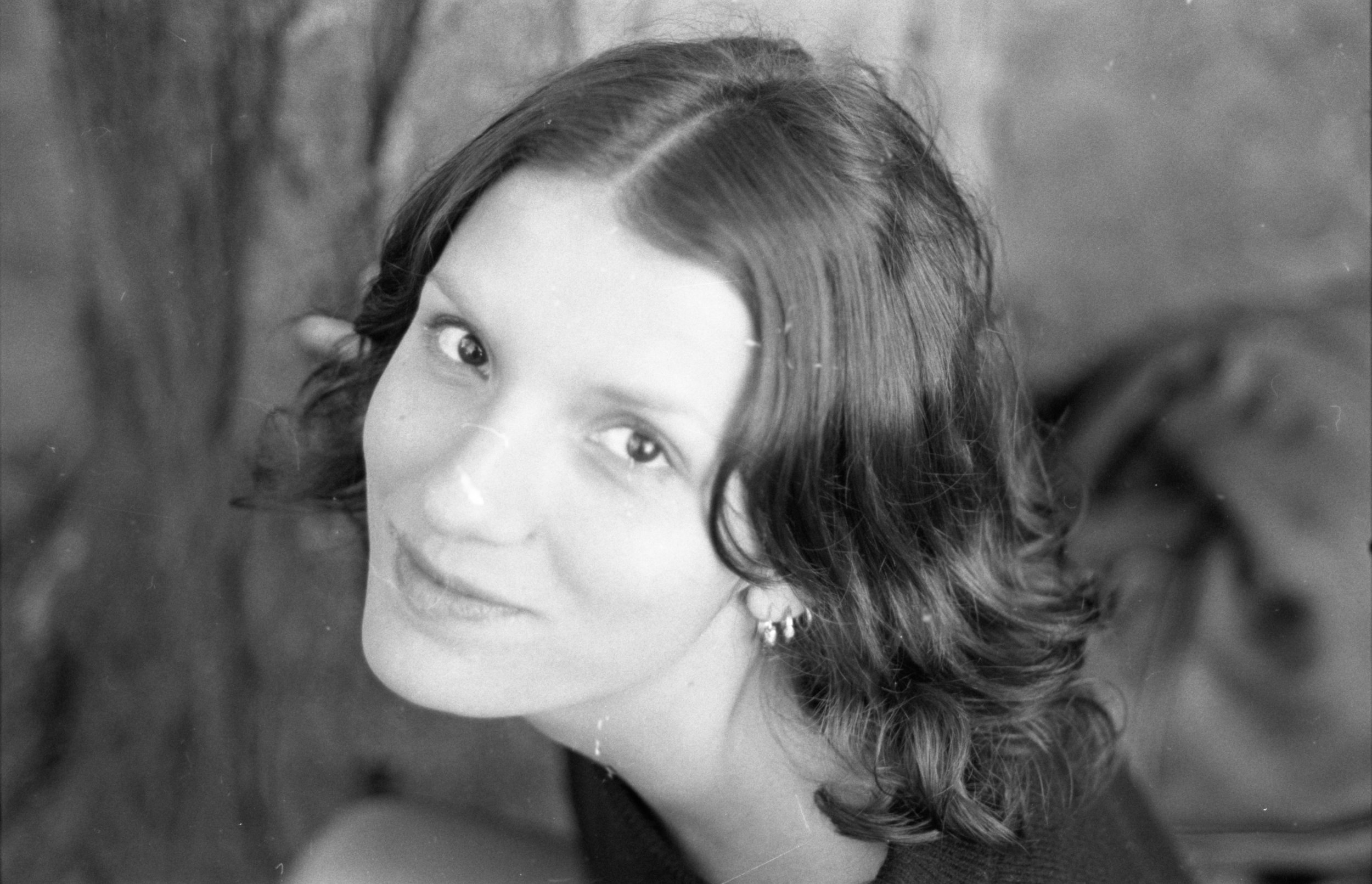 Black and white portrait of a young woman with wavy hair, wearing earrings, looking slightly upward with a subtle smile.