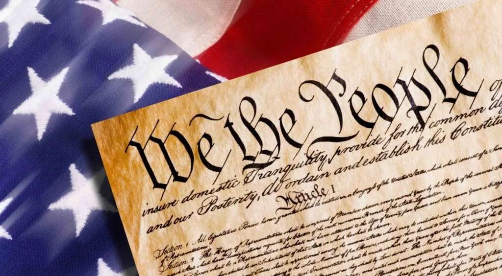 Close-up of the U.S. Constitution with American flag in the background.