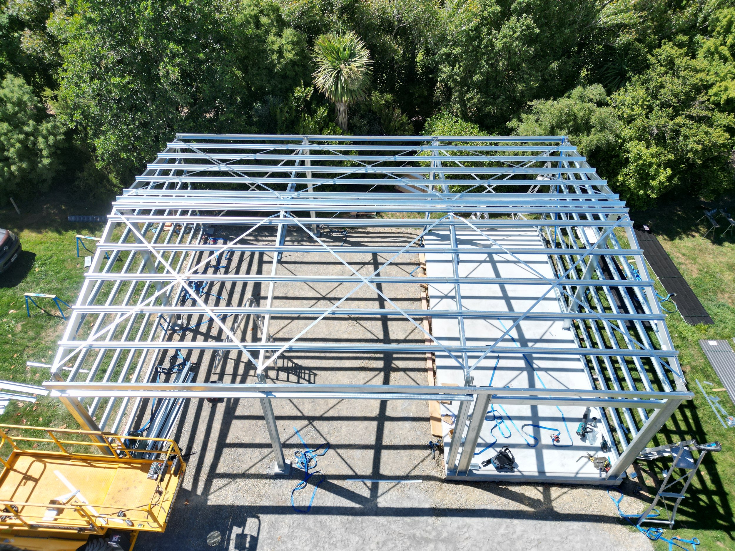 Aerial view of a building under construction with a metal frame structure in a green outdoor area.