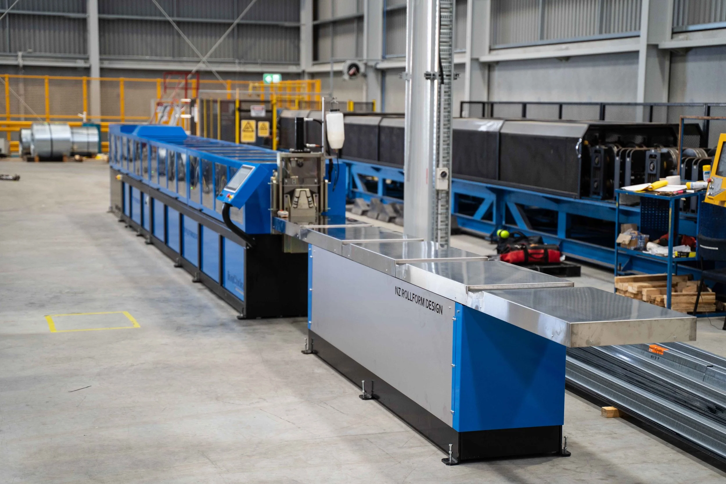 A Cold rolled steel frame machine in a warehouse, with a control panel, some tools, and materials nearby.
