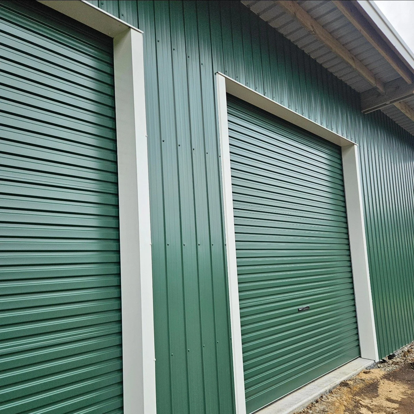 Green metal storage unit with rolling door, white trim, and a partial view of the building's underside roof.