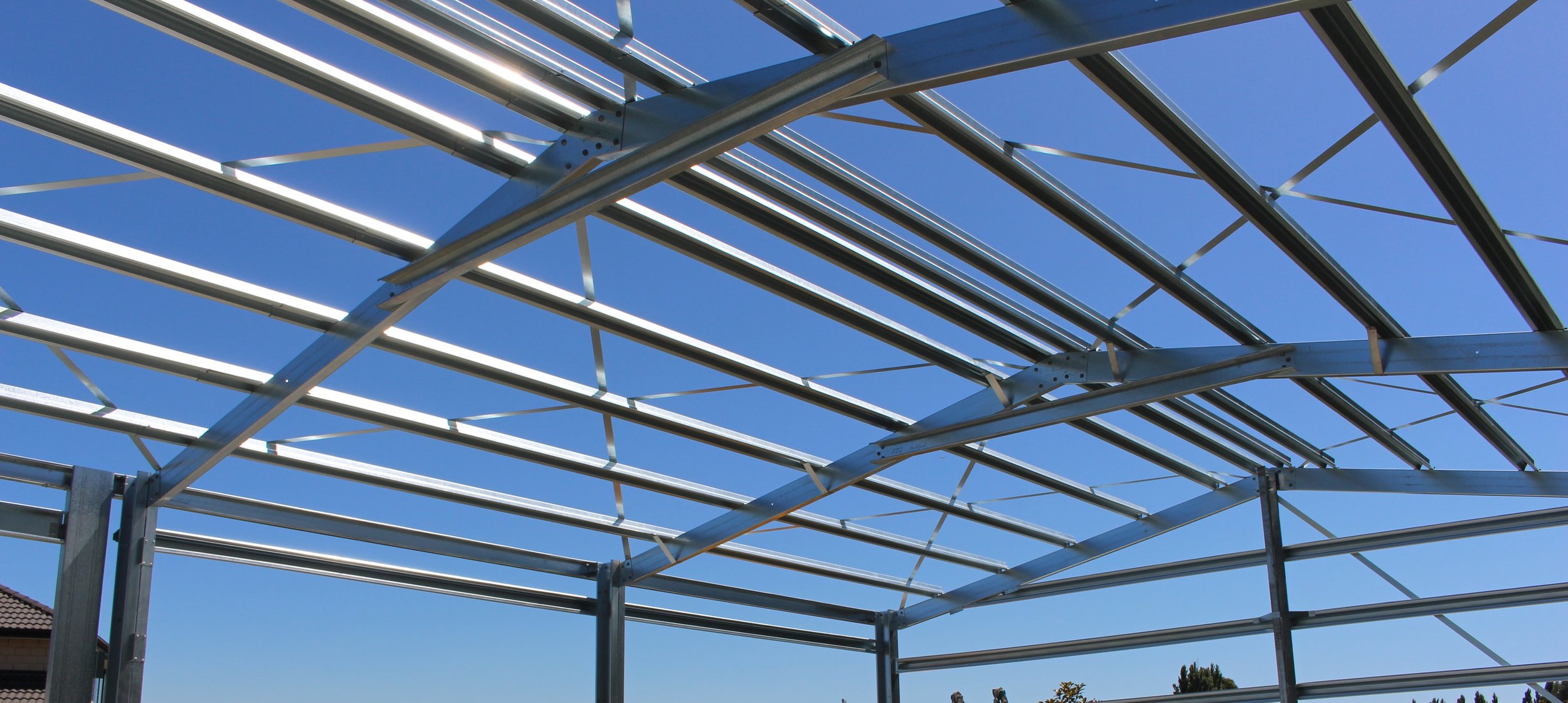 Metal framework of a Steel frame barn under construction against a clear blue sky.