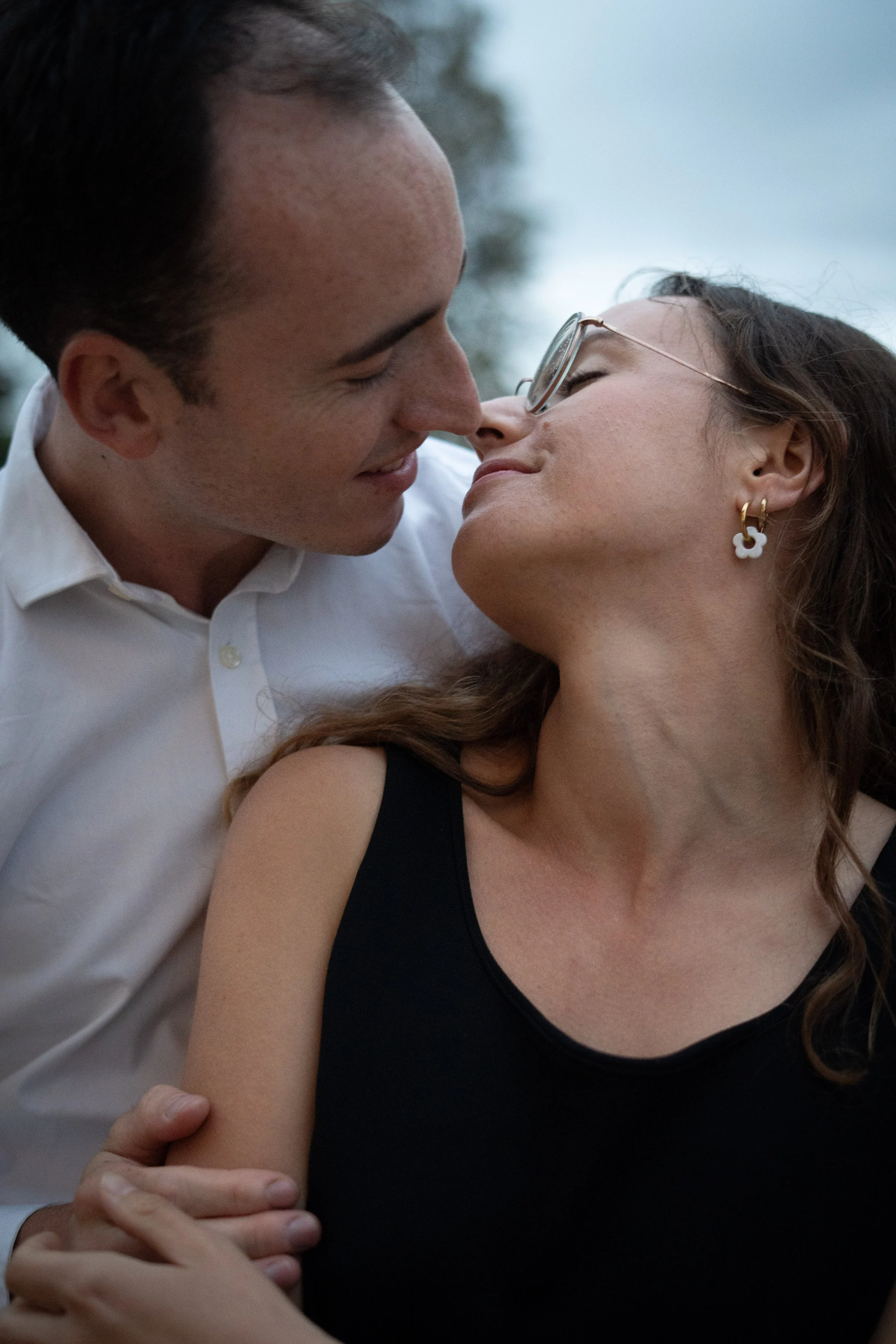 Un couple s'apprête à s'embrasser, avec le visage de l'homme très proche de celui de la femme, tous deux souriants, dans un cadre naturel.