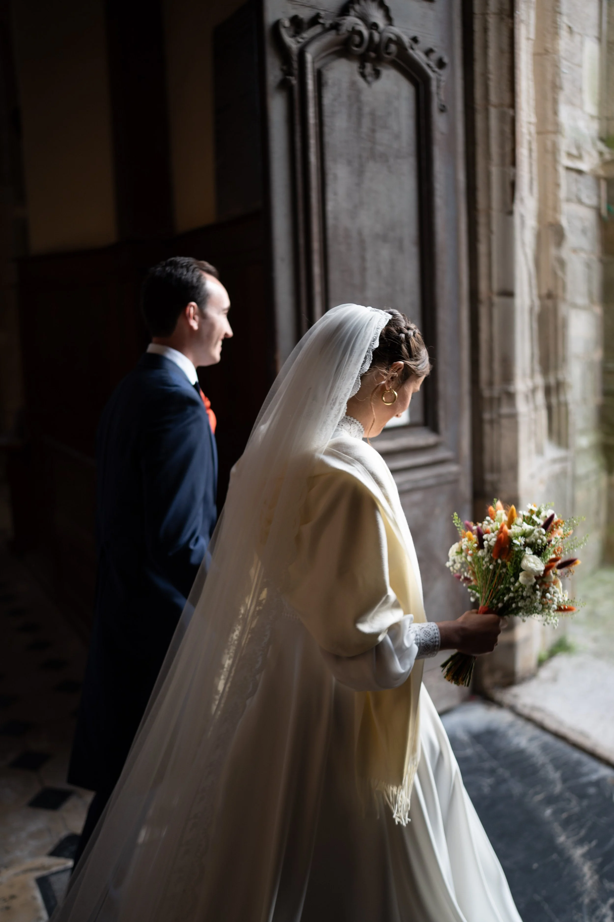 Un couple lors d'une cérémonie de mariage, sur le pas d'une église, la femme tenant un bouquet de fleurs, vue de profil