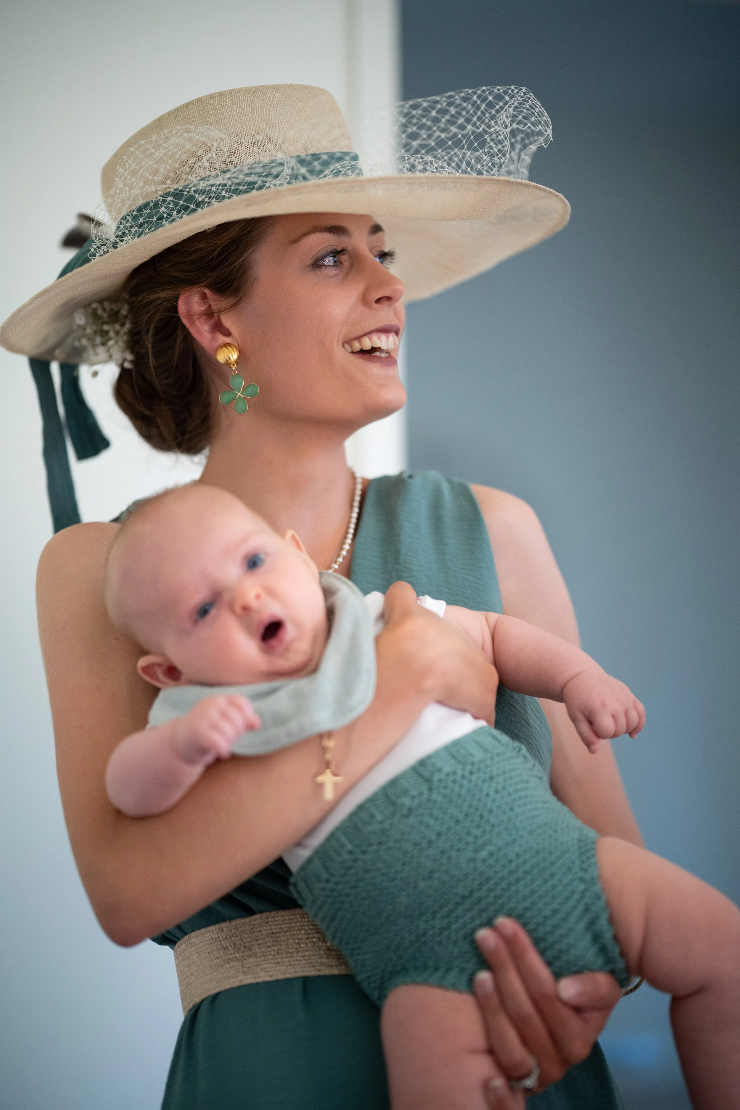 Une femme portant un chapeau élégant célèbre un moment joyeux avec un bébé qu'elle tient dans ses bras.