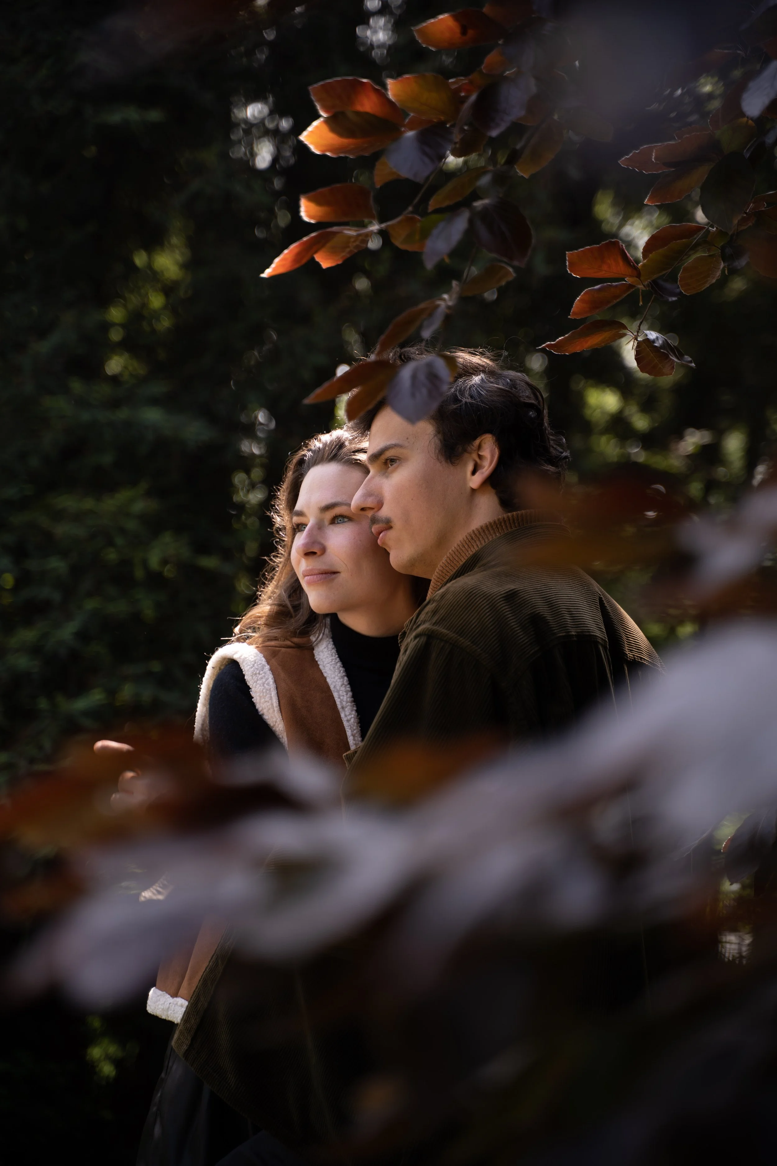 Un jeune homme et une jeune femme regardent tous les deux dans la même direction dans un environnement forestier, entourés de feuilles automnales.