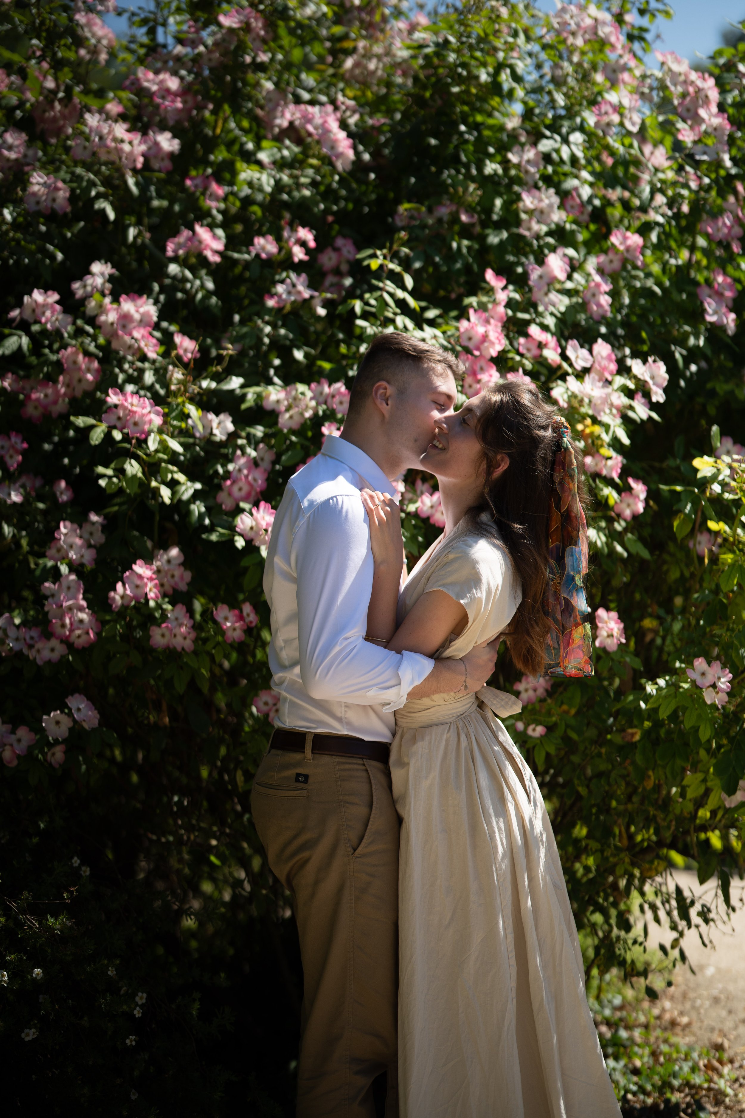 Un couple s'embrasse tendrement sous un arbre en fleurs, en pleine nature, par une journée ensoleillée.