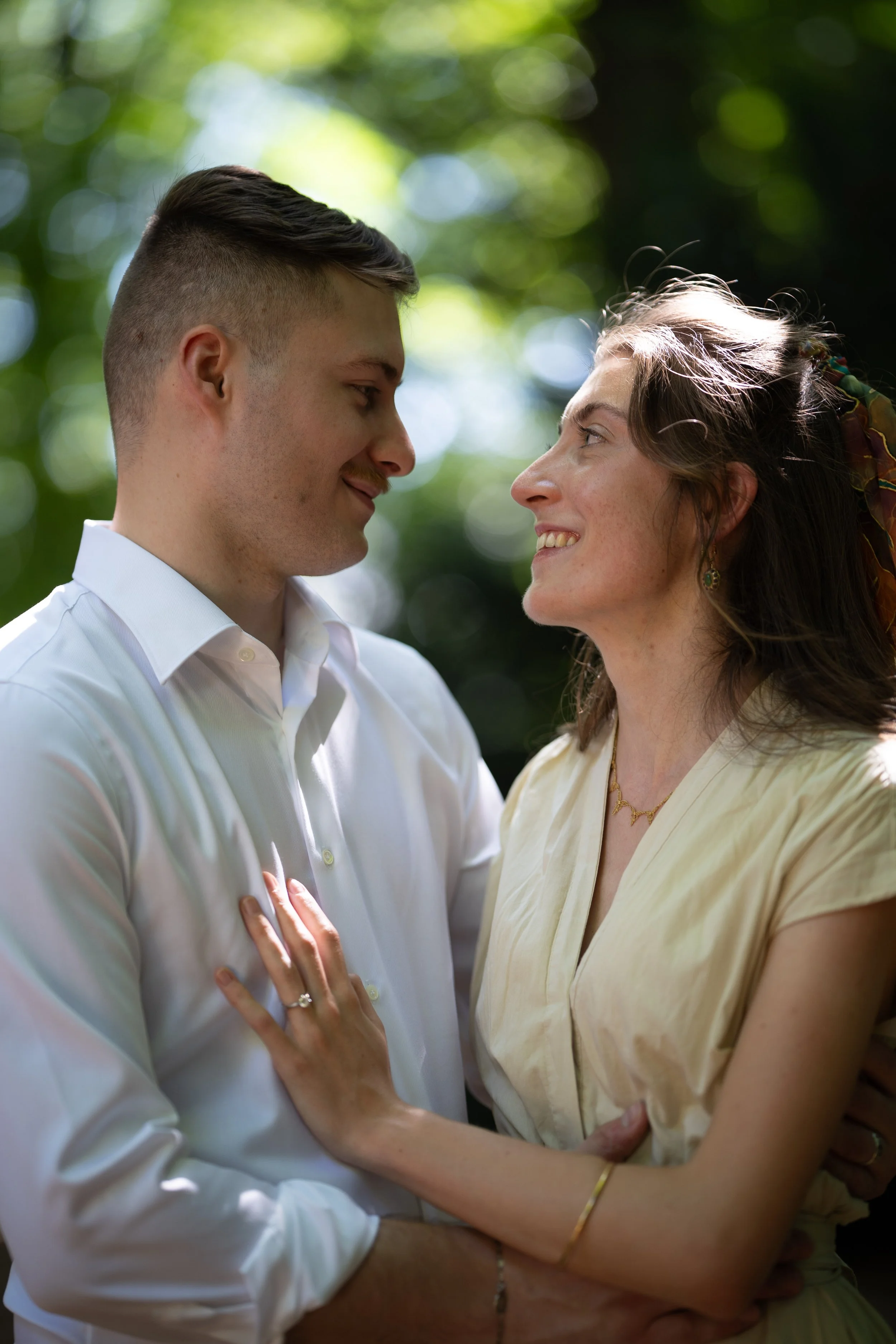 Un jeune homme et une femme âgée se regardent tendrement, souriant dans un cadre naturel avec des arbres en arrière-plan.