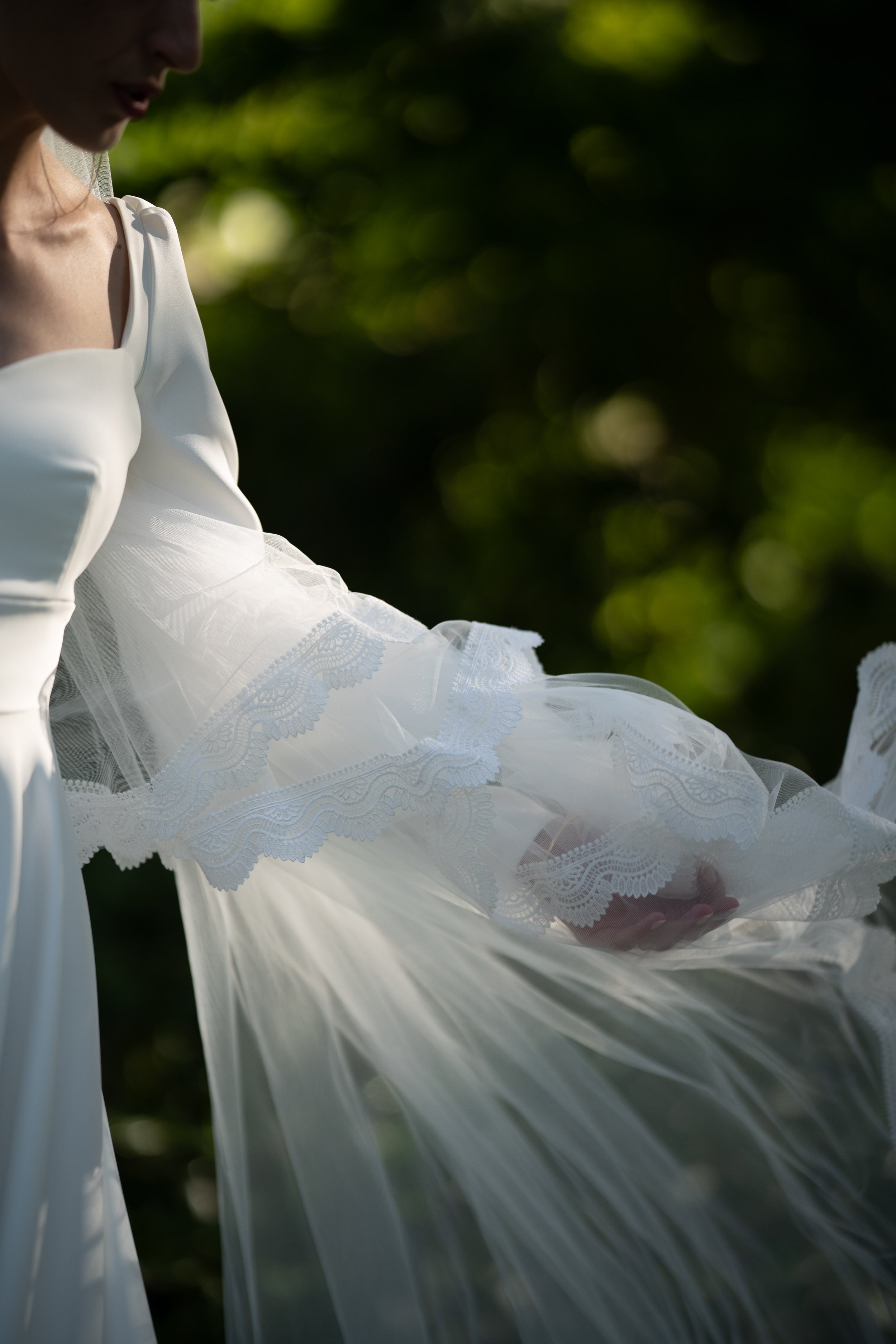 Femme en robe blanche avec des détails en dentelle, regardant vers le bas, avec un fond de nature flou.