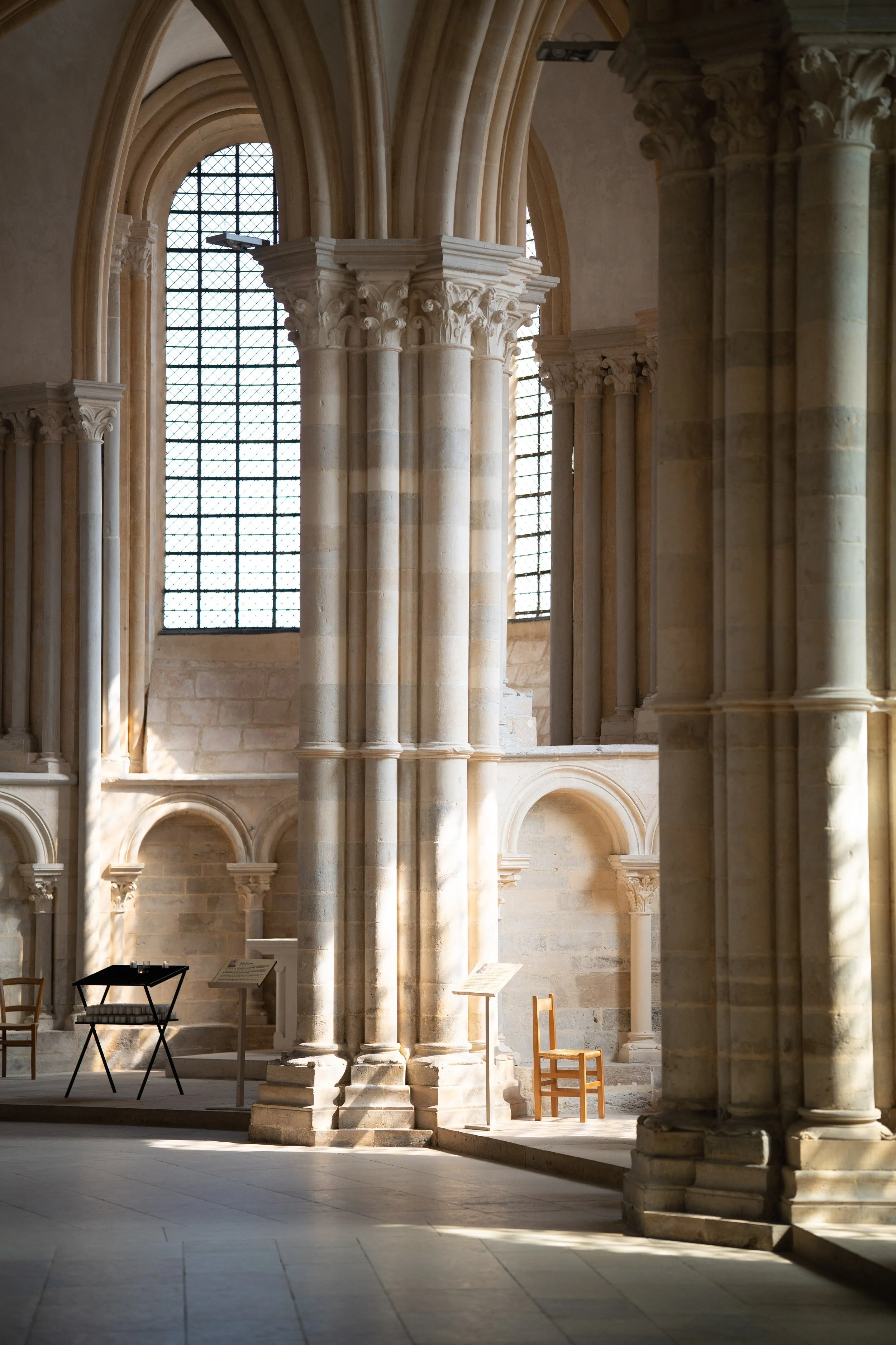 Intérieur d'une ancienne église avec des colonnes en pierre, vitraux et quelques meubles en bois et métal.