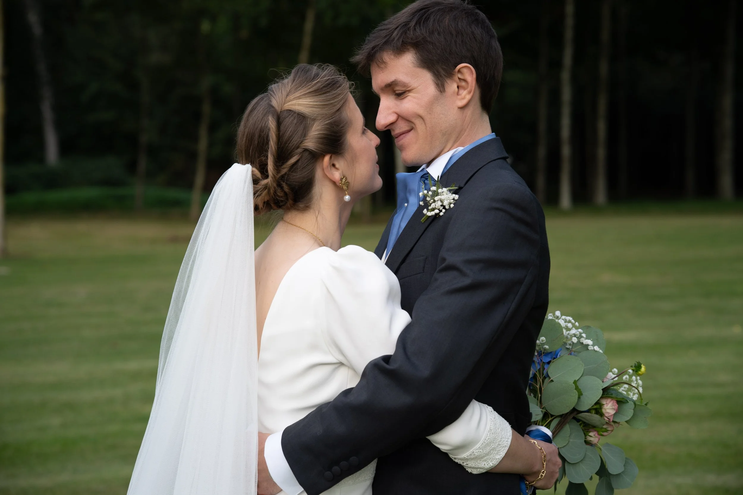 Un couple de mariés regarde tendrement au visage dans un cadre extérieur de jardin, lors de leur mariage.