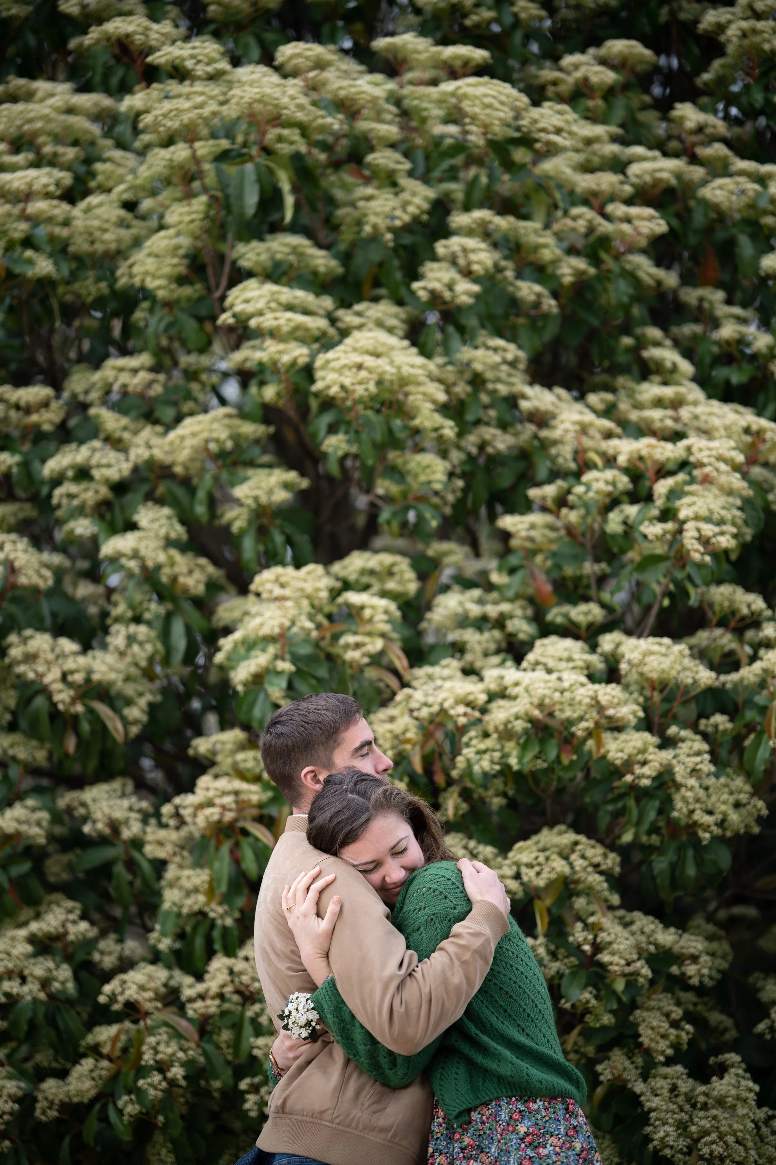 Un groupe de jeunes adultes en étreinte chaleureuse, en pleine nature devant un buisson de fleurs blanches.