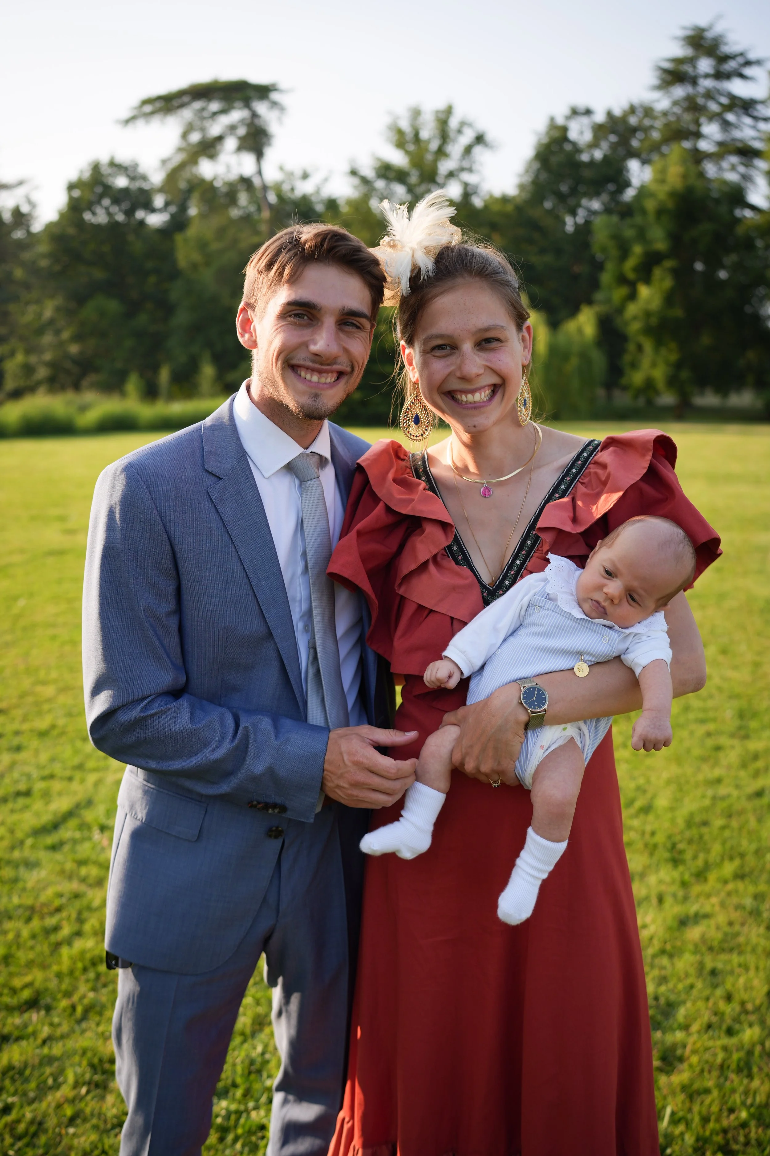 Un couple souriant avec un bébé dans un parc vert en plein air, lors d'une journée ensoleillée.
