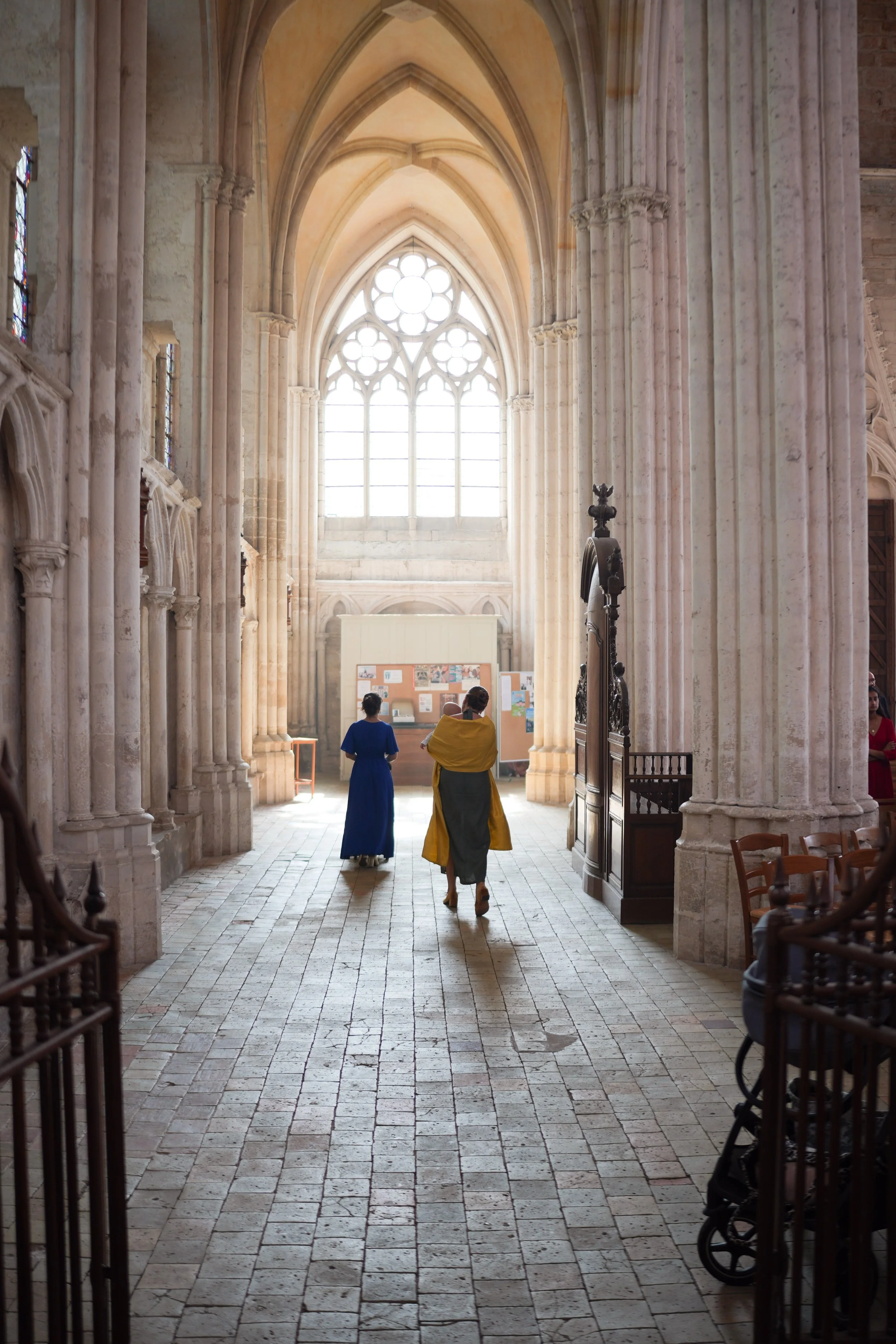 Intérieur d'une cathédrale avec des vitraux colorés, des colonnes en pierre et des personnes marchant dans l'allée centrale.