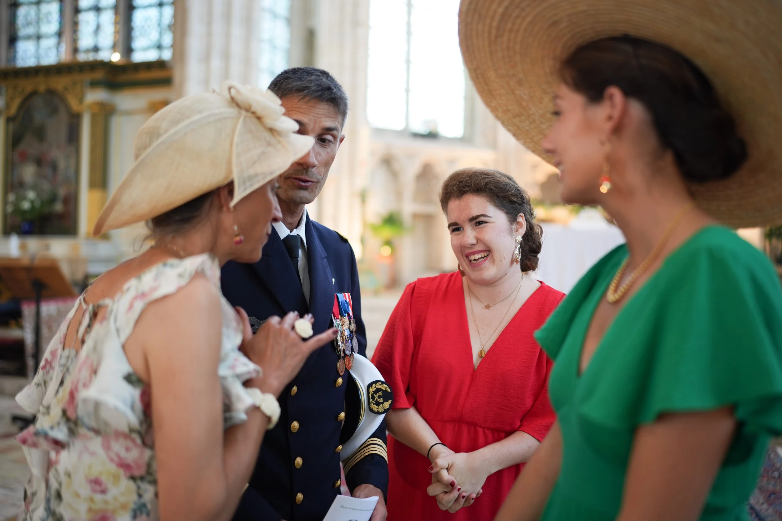 Groupe de quatre personnes, deux femmes et deux hommes, lors d'une cérémonie, probablement une cérémonie officielle ou une commémoration. Les femmes portent des chapeaux élégants et des vêtements colorés, et l'homme porte un uniforme avec des médaill