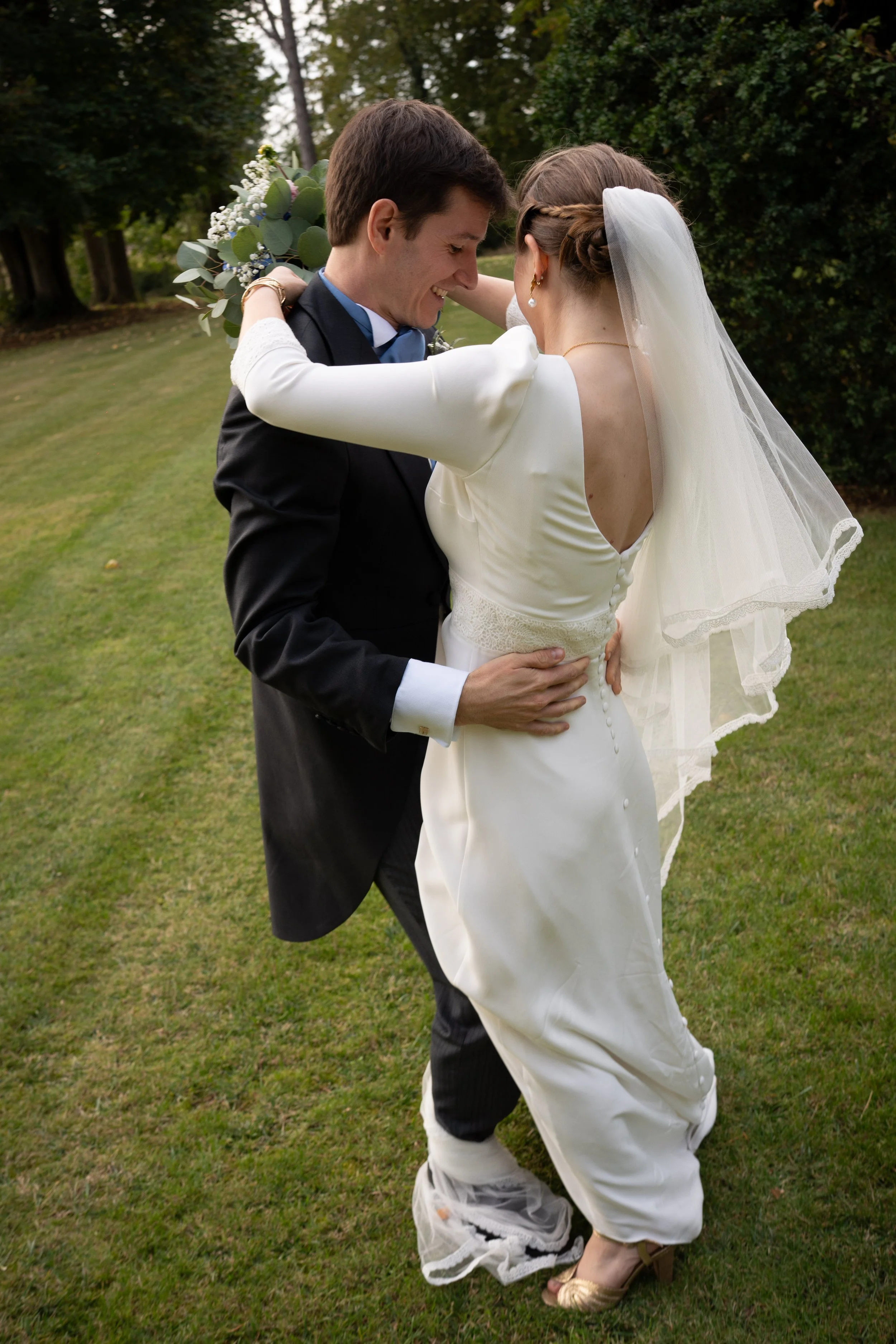 Un couple habillé en tenue de mariage dansant sur une pelouse verte, entouré d'arbres.