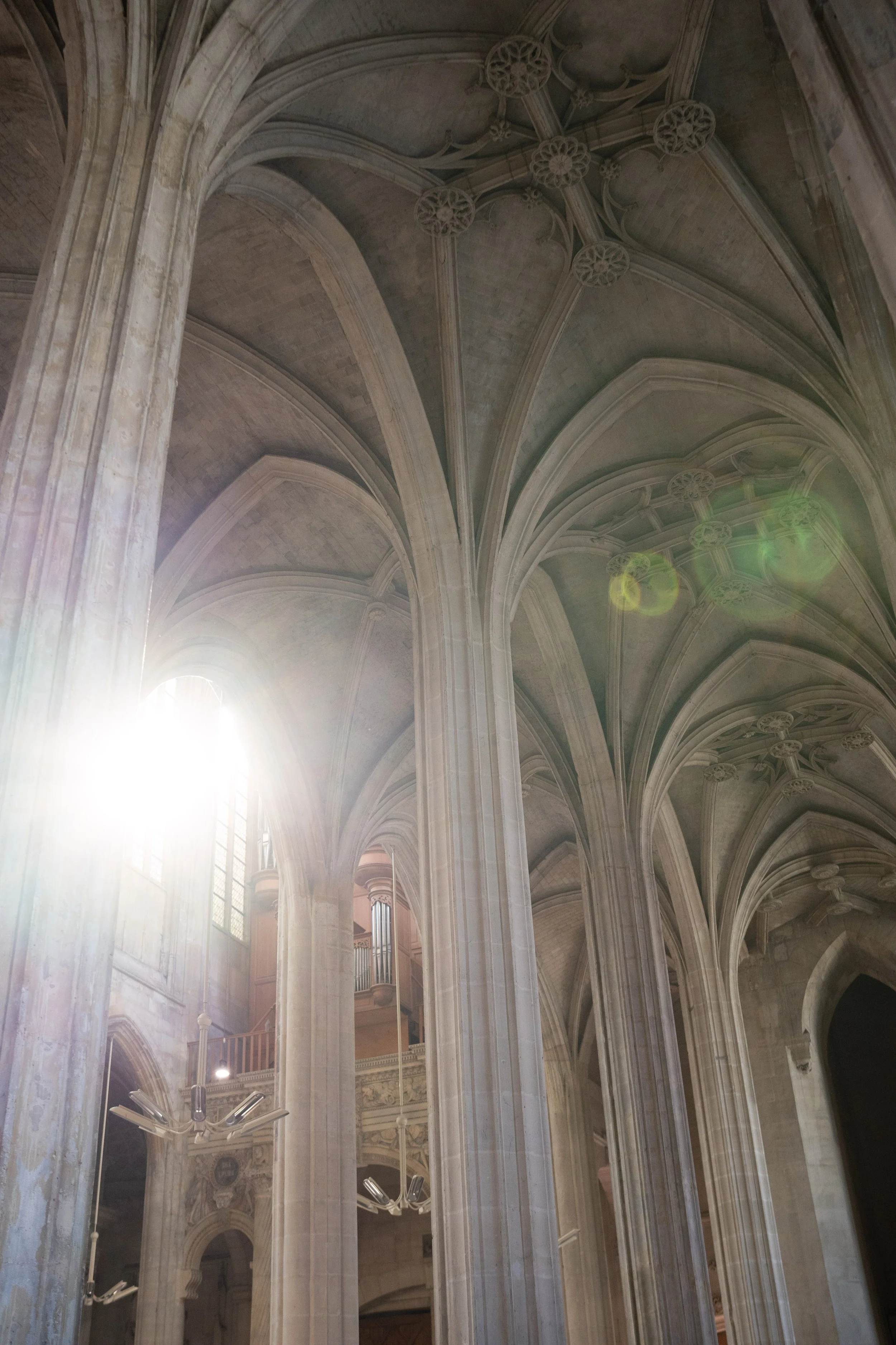 Intérieur d'une grande église ou cathédrale avec des arches gothiques en pierre, une lumière naturelle qui entre par une fenêtre au fond et un plafond voûté richement décoré.