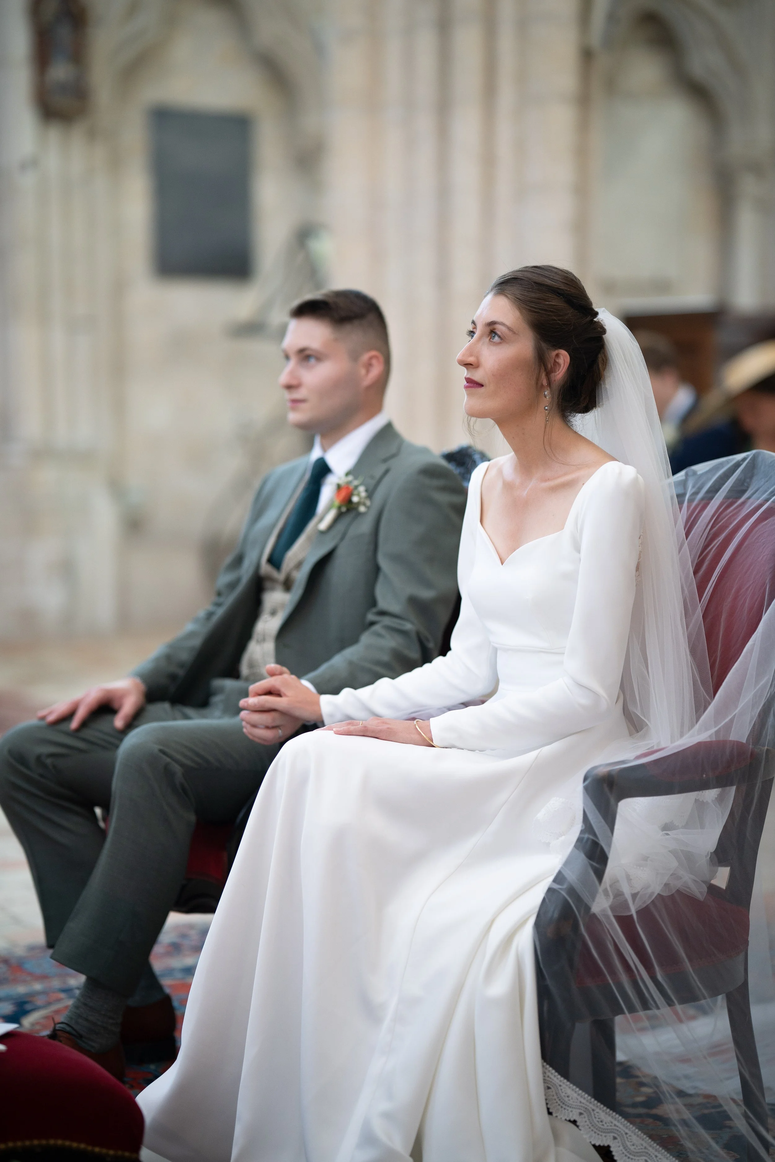 Un couple en robe de mariée et costume assis dans une église lors d'une cérémonie nuptiale.