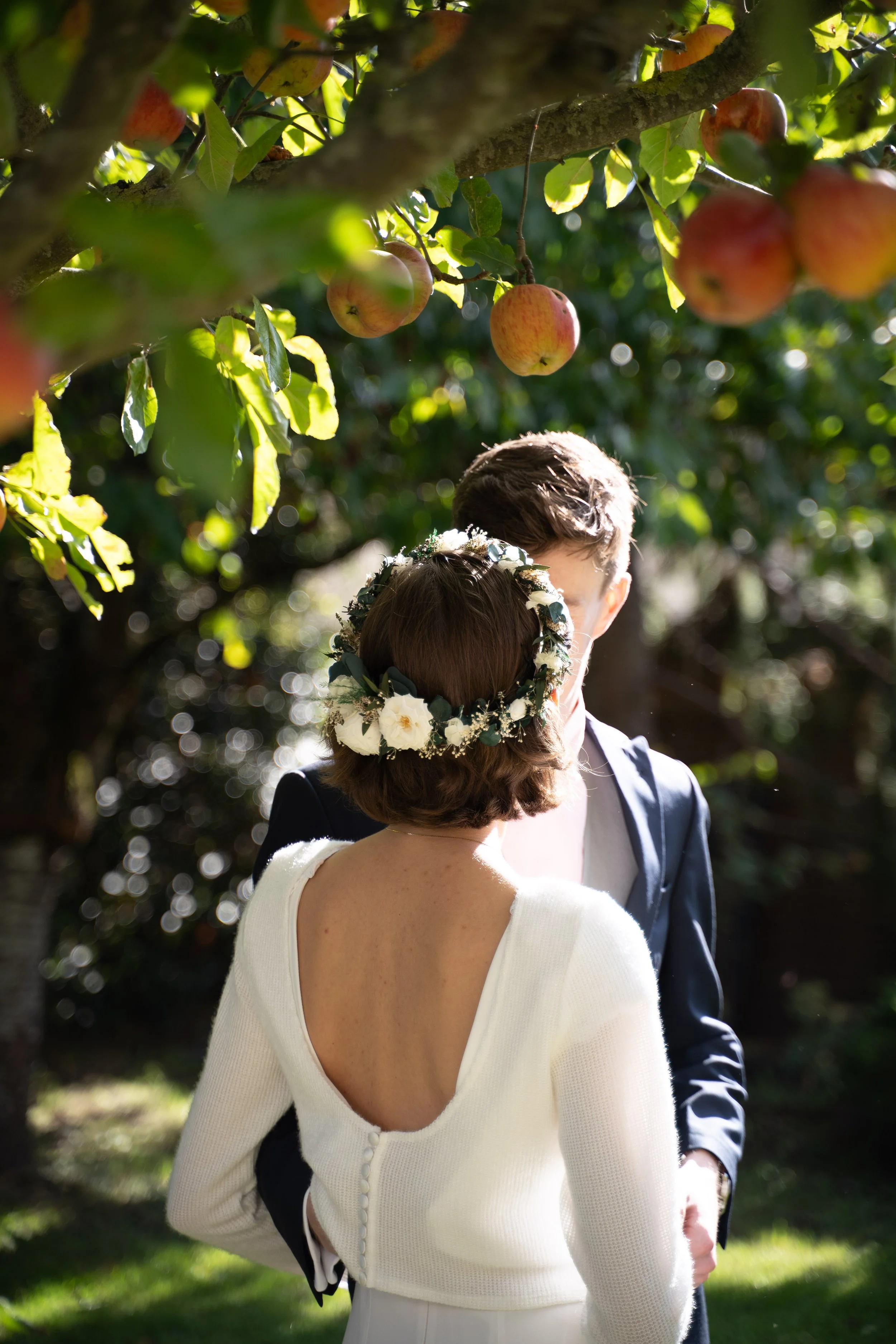 Deux personnes se tenant par la main lors d'une cérémonie de mariage en extérieur, avec des arbres et des pommes suspendues en arrière-plan.