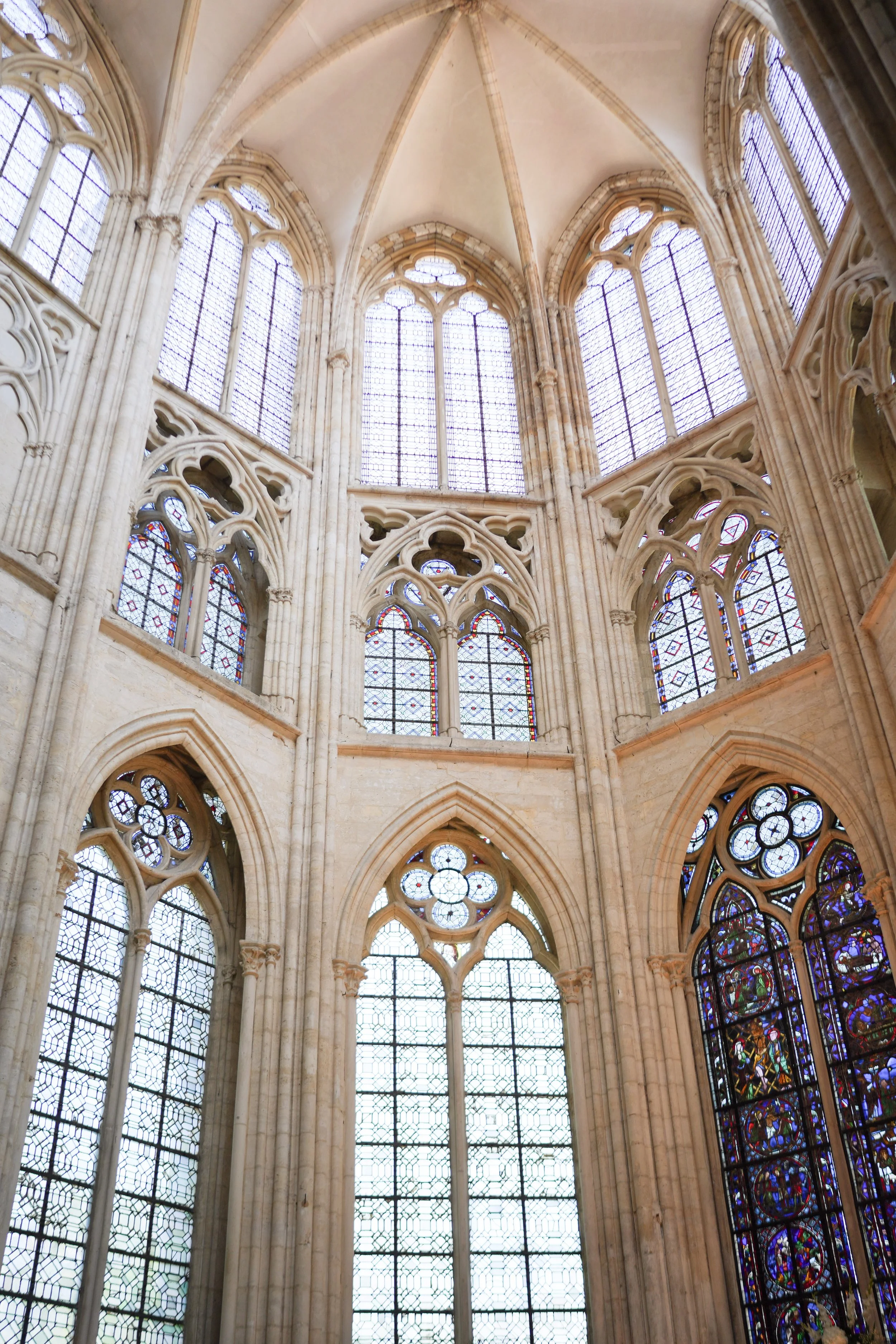 Intérieur d'une cathédrale gothique avec de grandes fenêtres en vitrail, voûtes en arche et architecture en pierre.