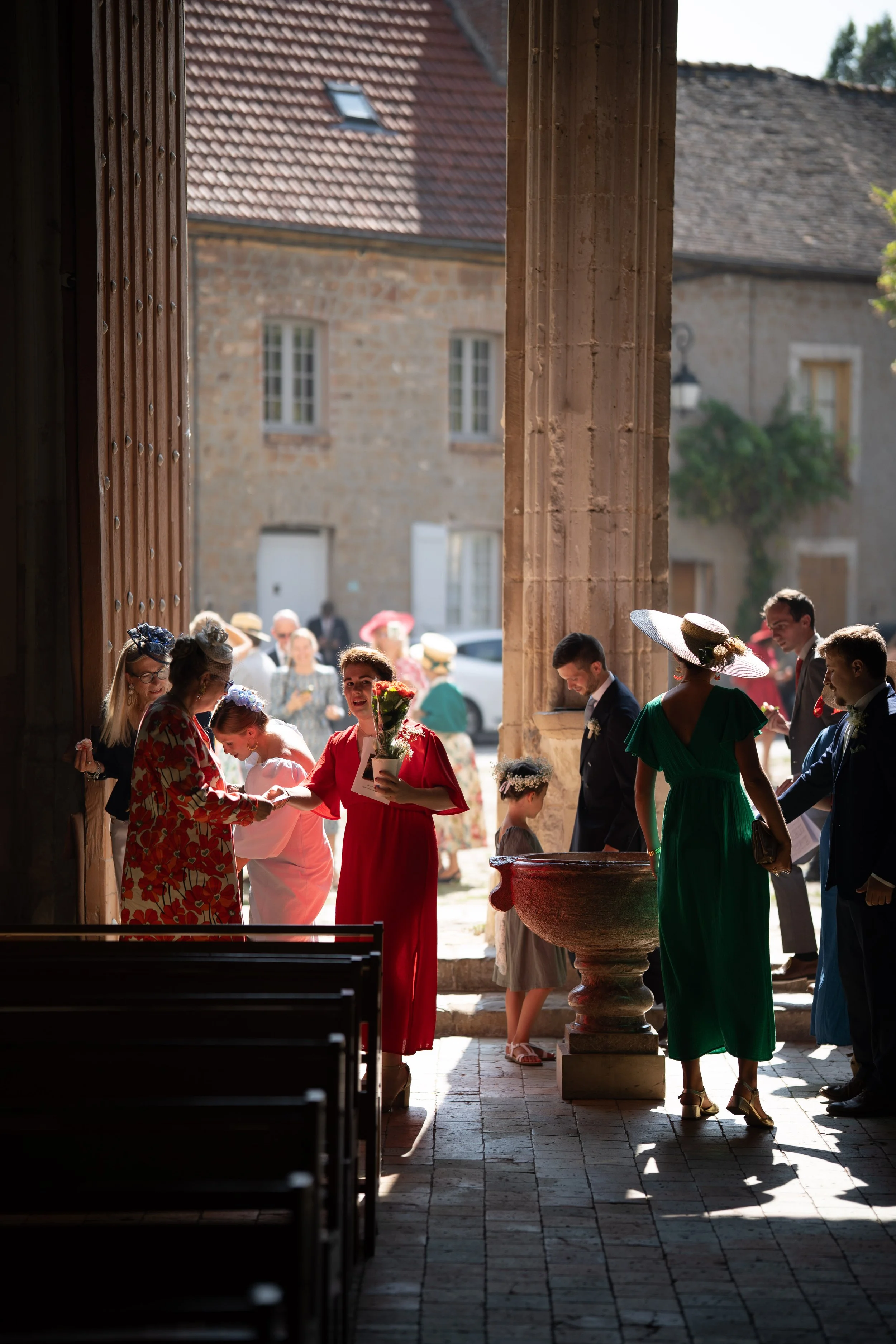Groupe de personnes lors d'un mariage, proche d'une fontaine, dans une architecture en pierre avec des fenêtres blanches, sous un portique en pierre.