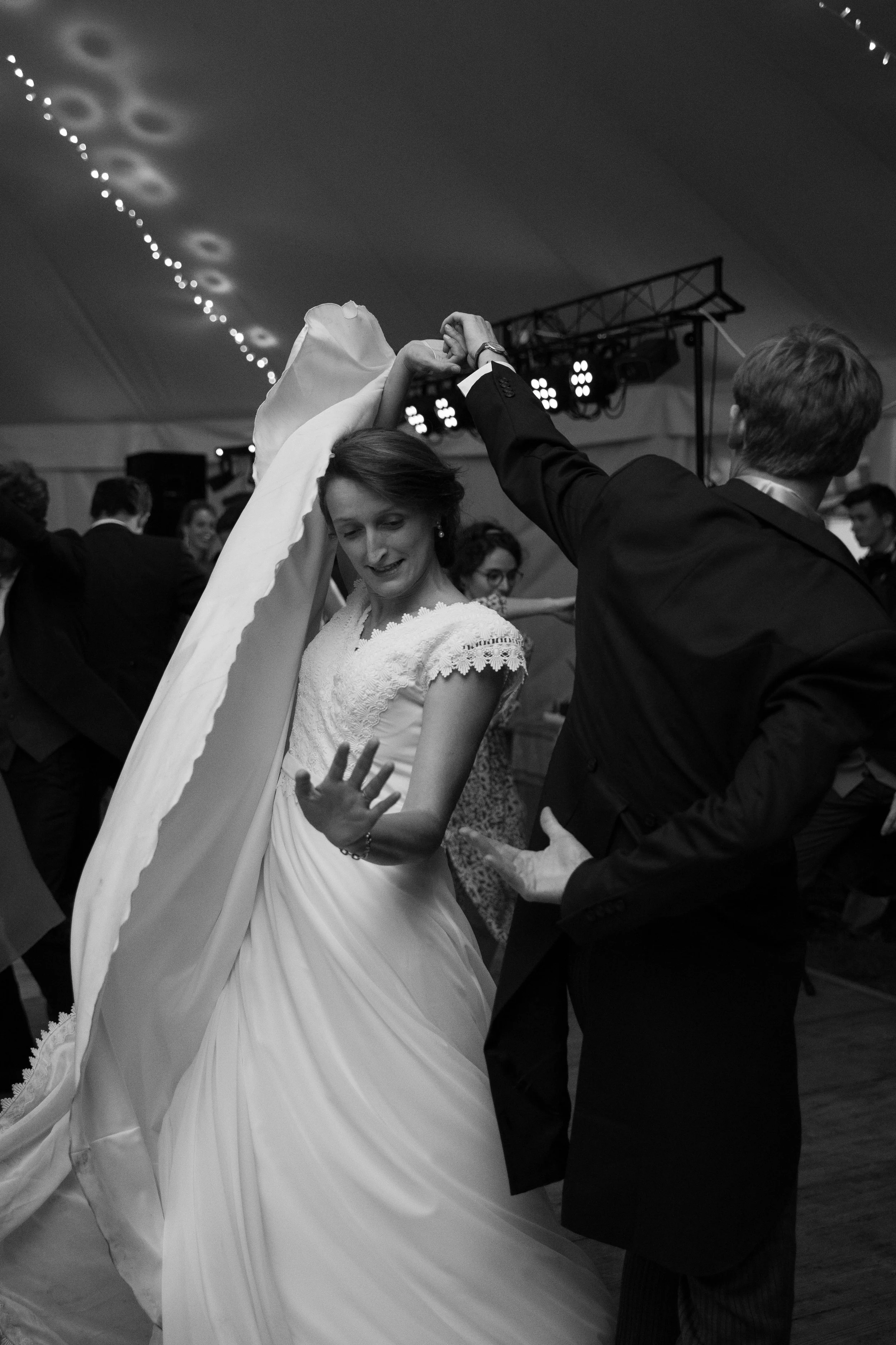 Un couple dansant lors d'une fête ou d'un mariage, en noir et blanc, avec d'autres personnes en arrière-plan.