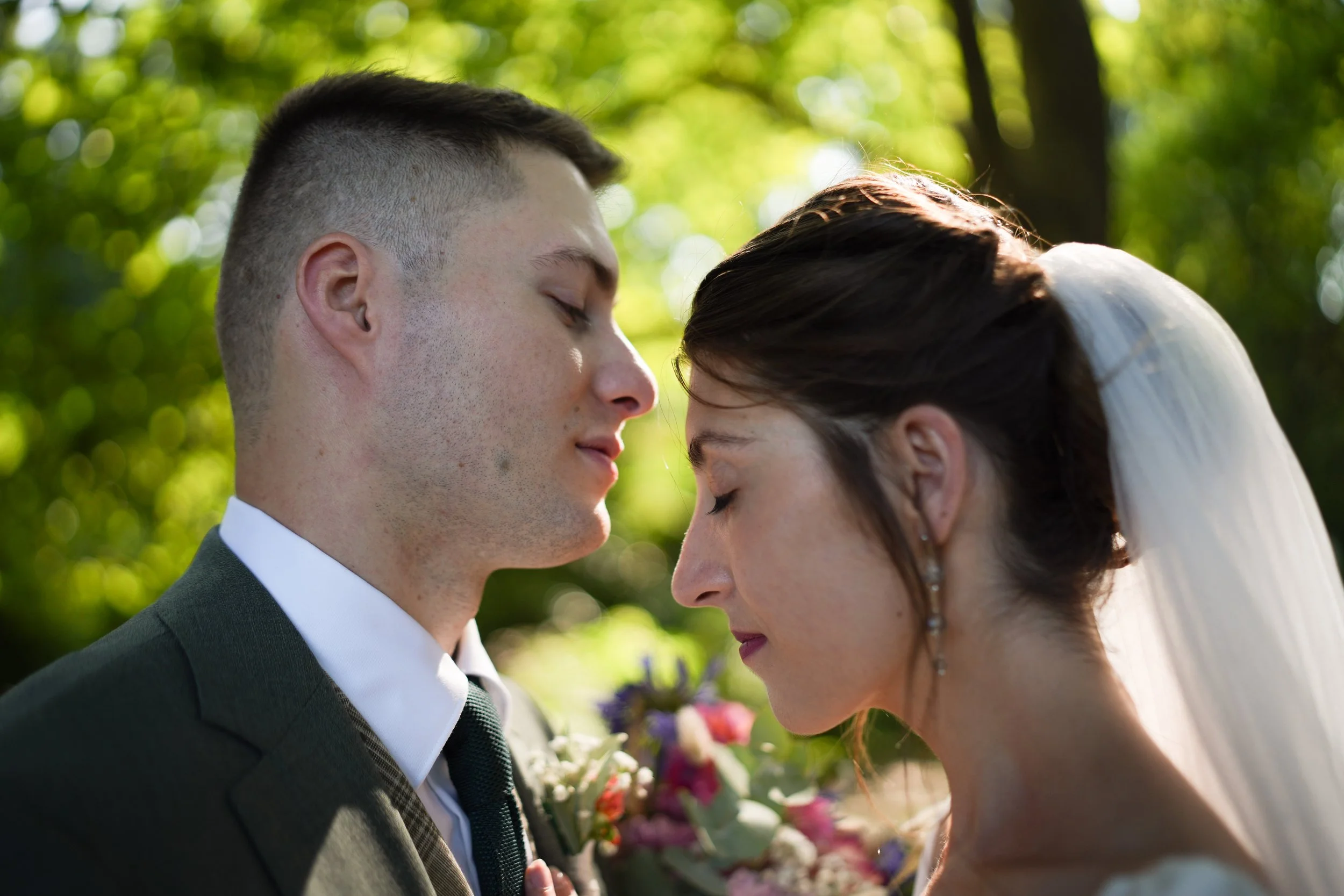 Un couple de mariés s'embrassent tendrement lors de leur mariage en plein air, avec un fond de nature verdoyante.