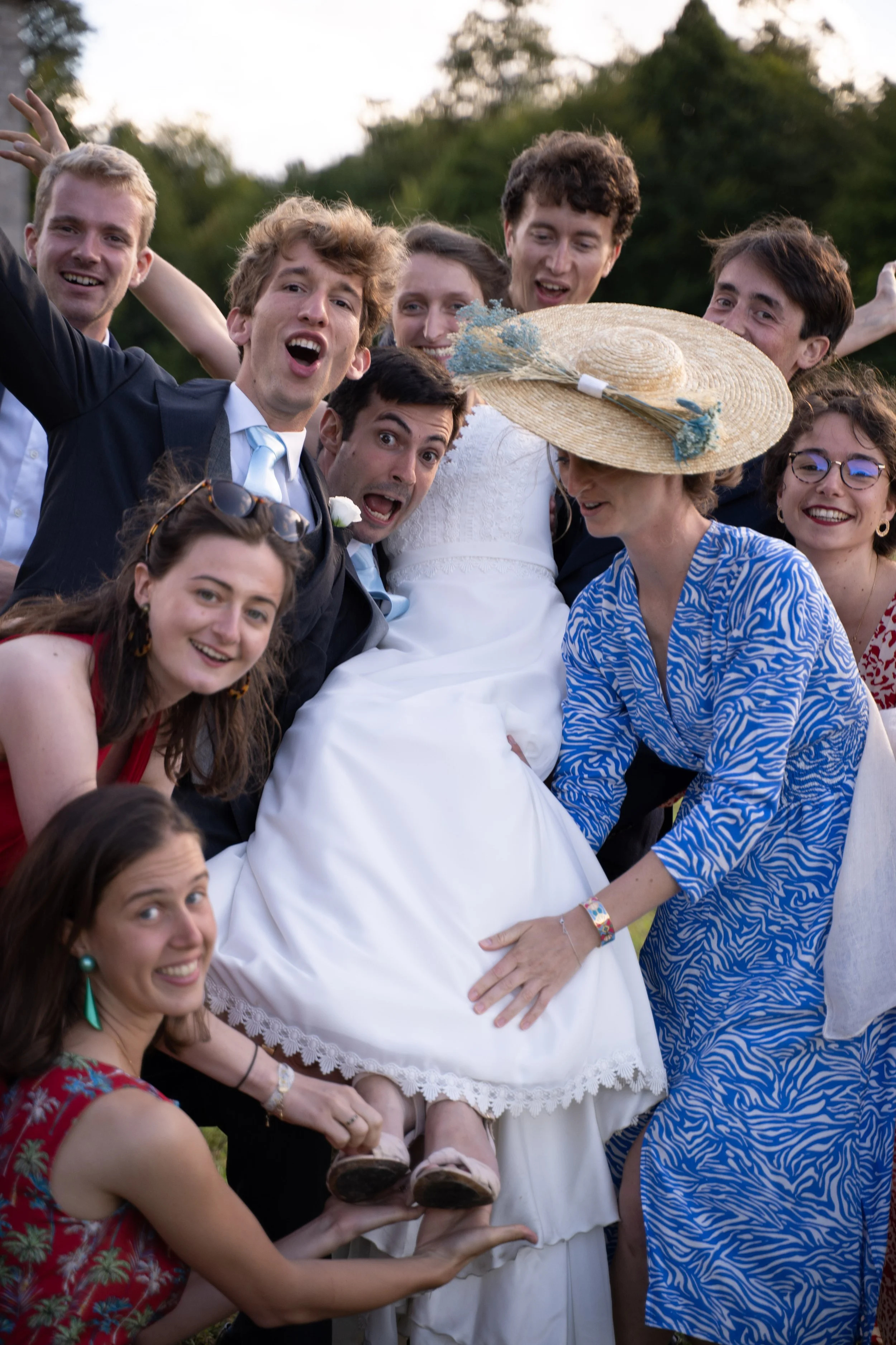 Un groupe de jeunes souriants posent pour une photo lors d'une célébration en plein air, avec une femme portant un grand chapeau en paille au centre.