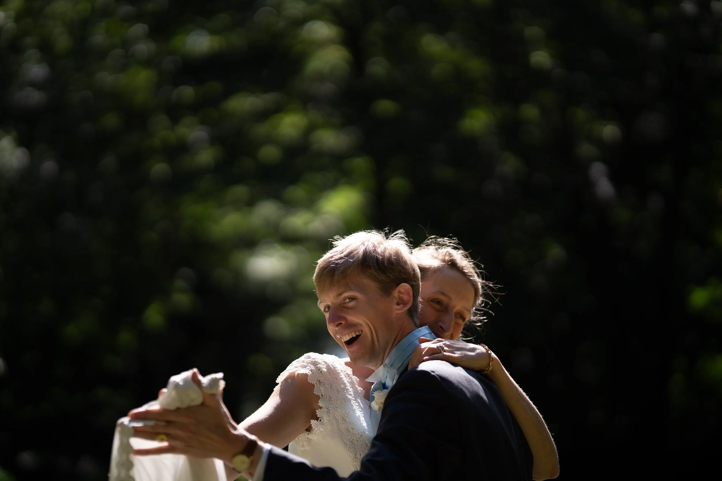 Deux personnes dansent et sourient lors d'une cérémonie en plein air, avec des arbres en arrière-plan, une femme en robe blanche et un homme en costume