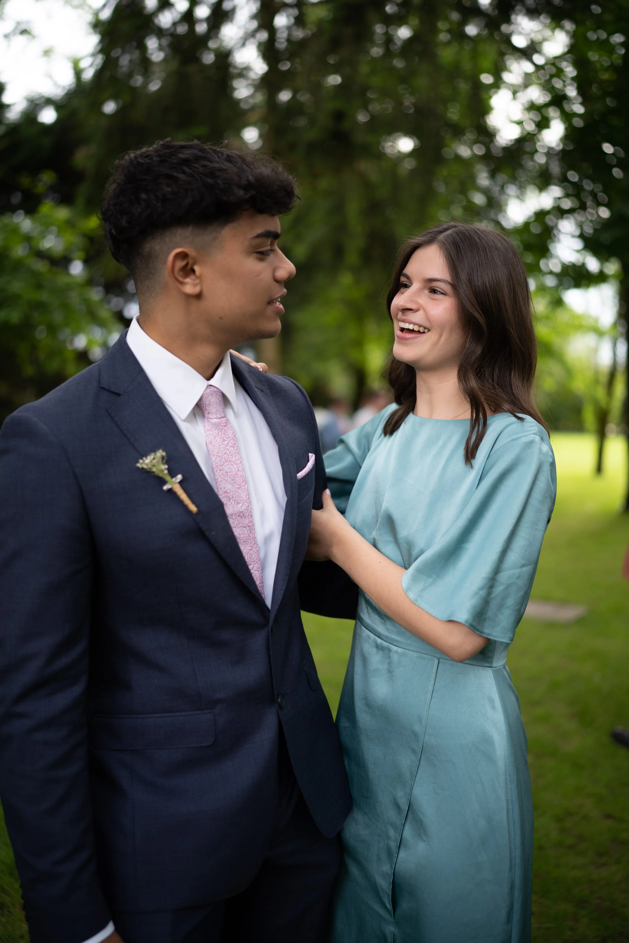 Un couple en tenue formelle partage un moment heureux dans un parc verdoyant.