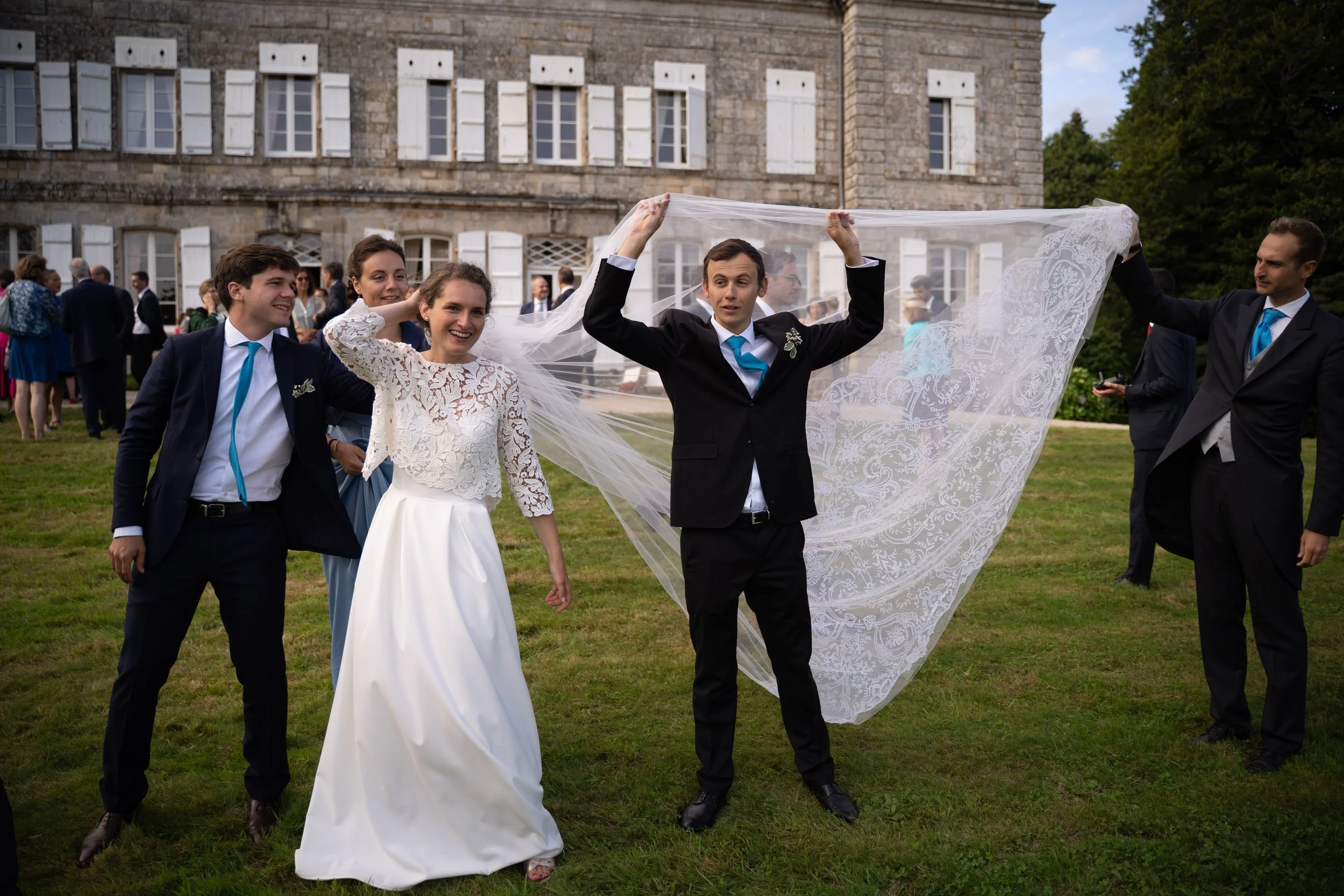 Groupe de personnes lors d'un mariage, avec un homme en costume noir avec une cravate bleue couvrant la mariée avec un voile en dentelle.