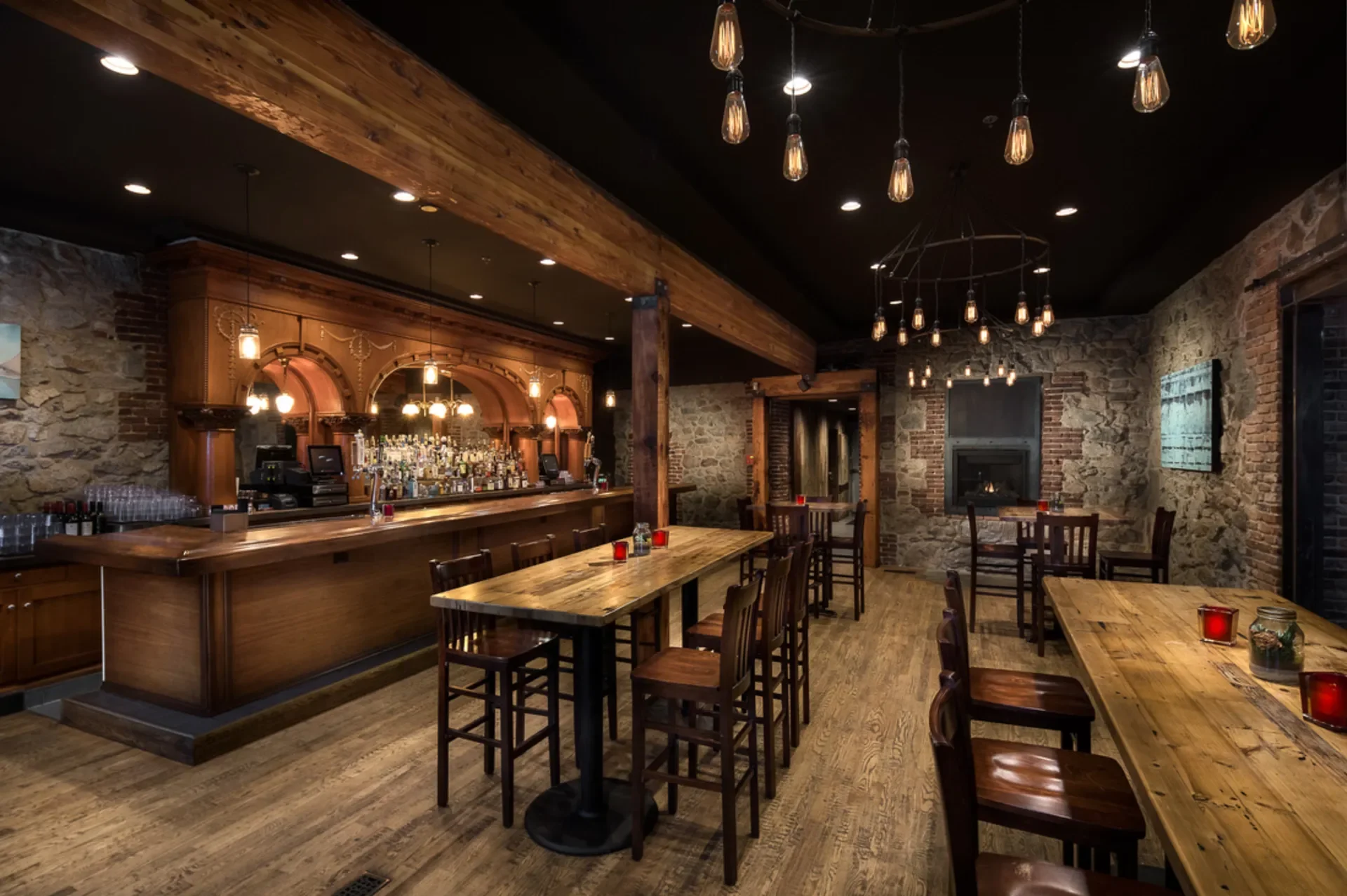 Interior view of a rustic bar and restaurant with wooden tables and chairs, stone walls, dim ambient lighting, and a fireplace