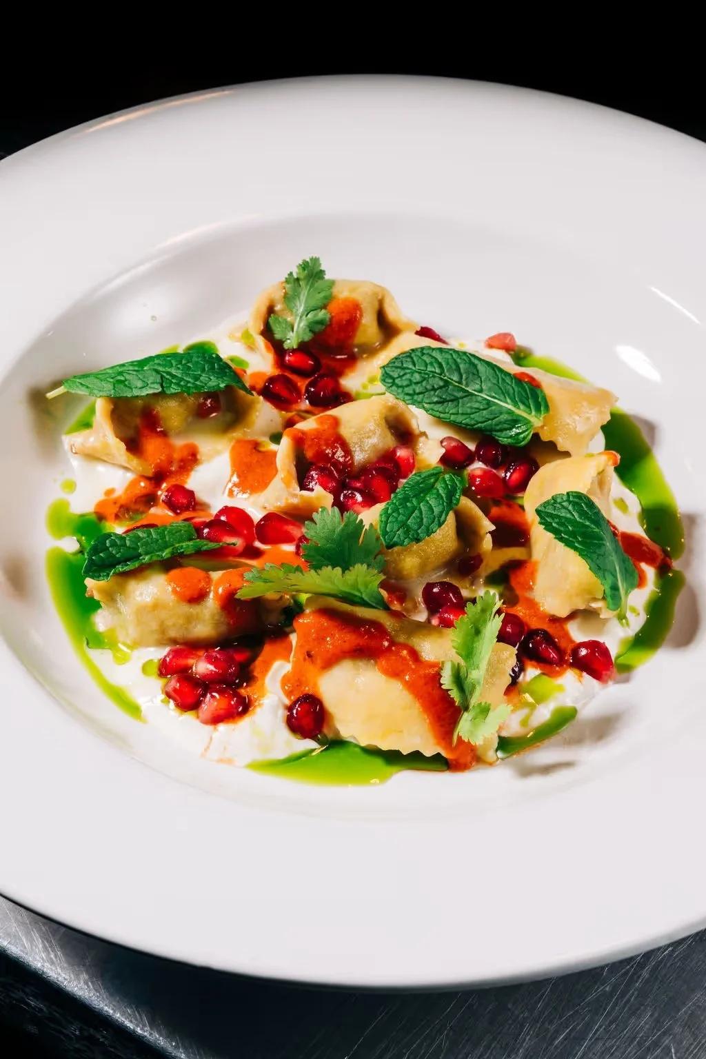Plate of ravioli garnished with pomegranate seeds, fresh herbs, and colorful sauces
