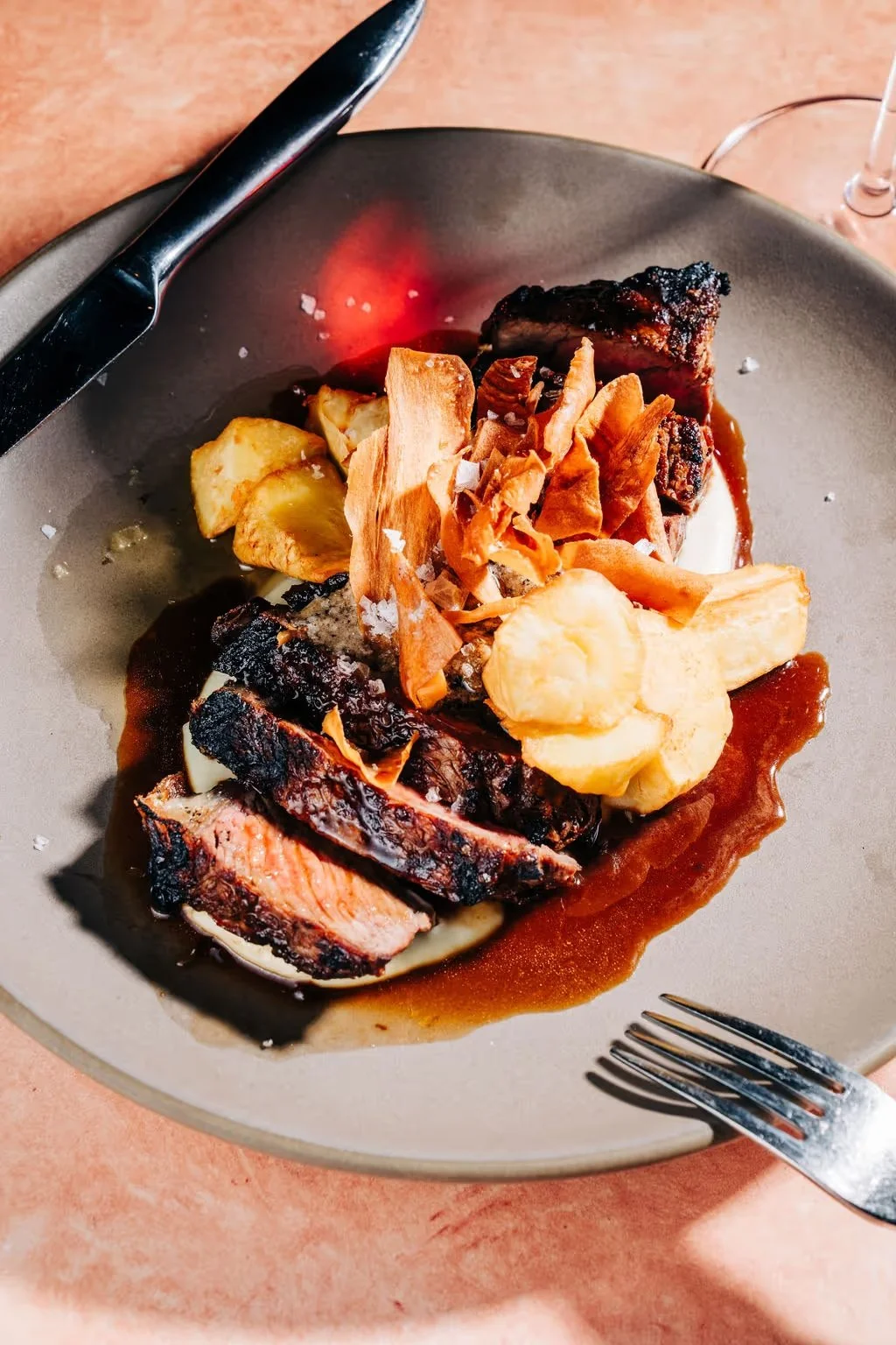 A plated meal featuring grilled meat, roasted potatoes, crispy onion toppings, and sauce, garnished with coarse salt.
