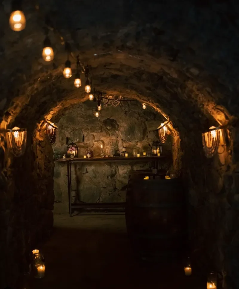 A dimly lit underground stone tunnel decorated with string lights, candles, and lanterns, creating a cozy and mysterious atmosphere.