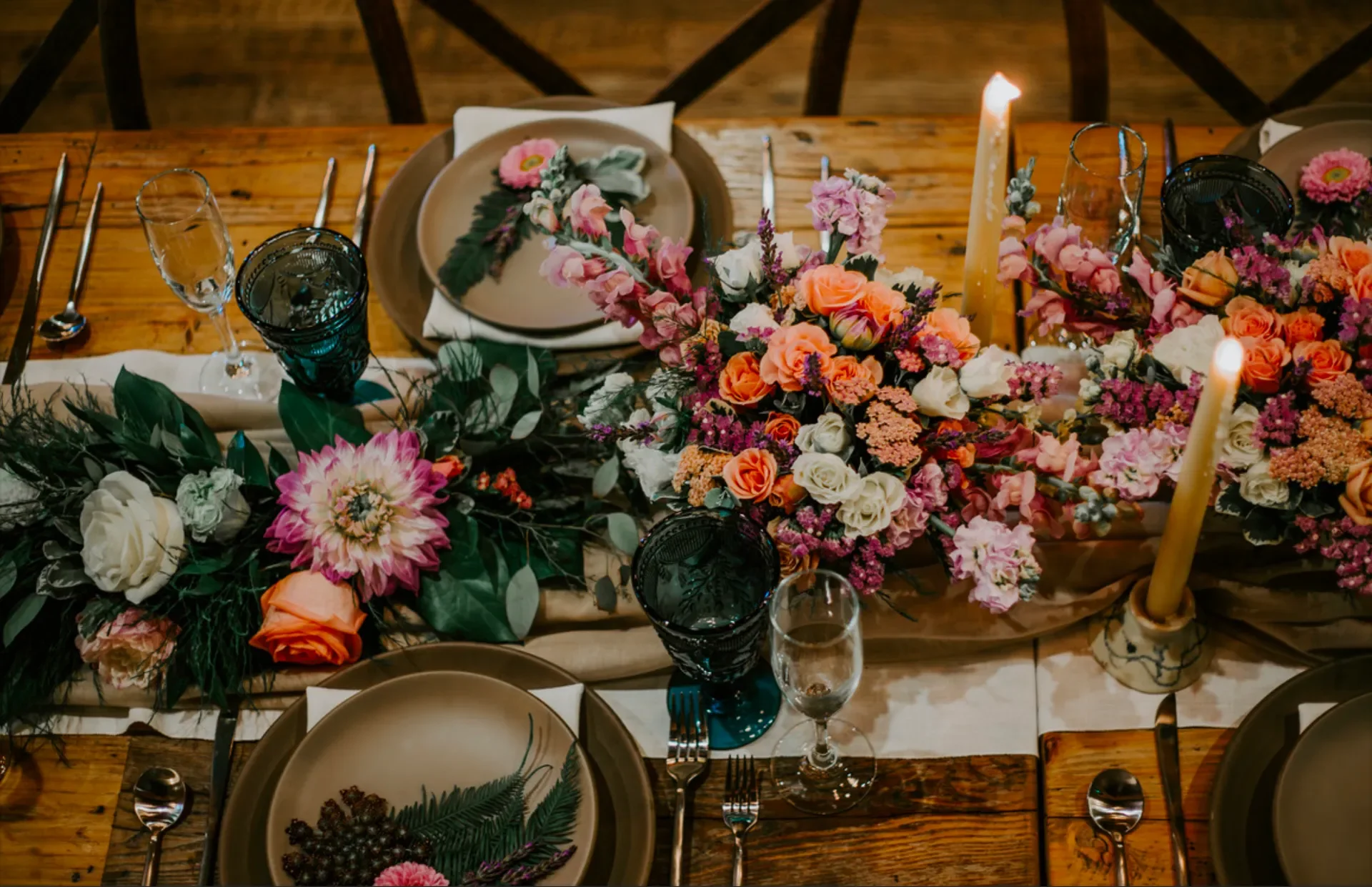 A wooden dining table set for a meal with floral arrangements, candles, and elegant dinnerware.