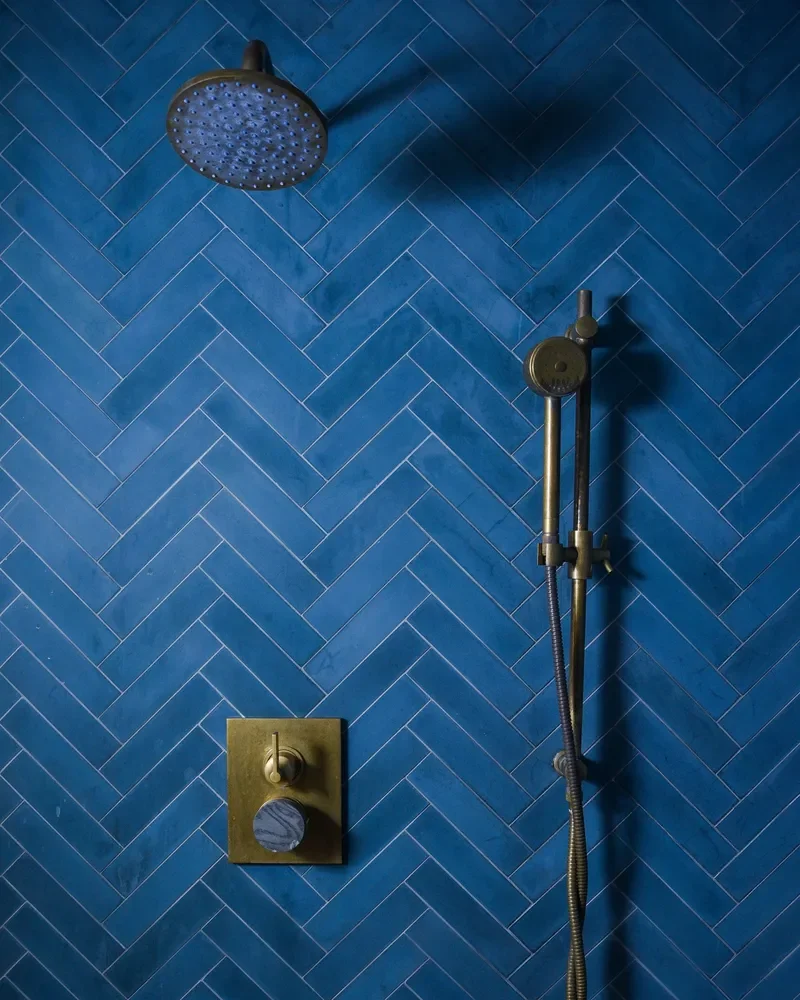 A modern showerhead and control valve on a blue tiled wall in a shower.