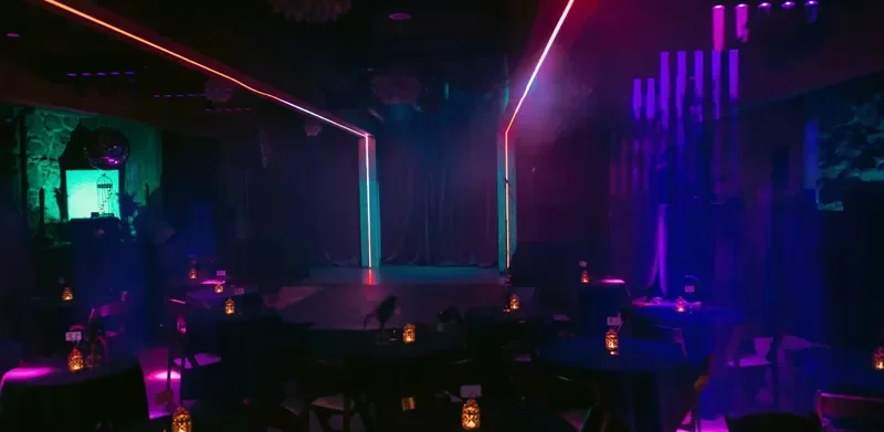 Empty nightclub with a stage, colorful neon lights, and tables with candles
