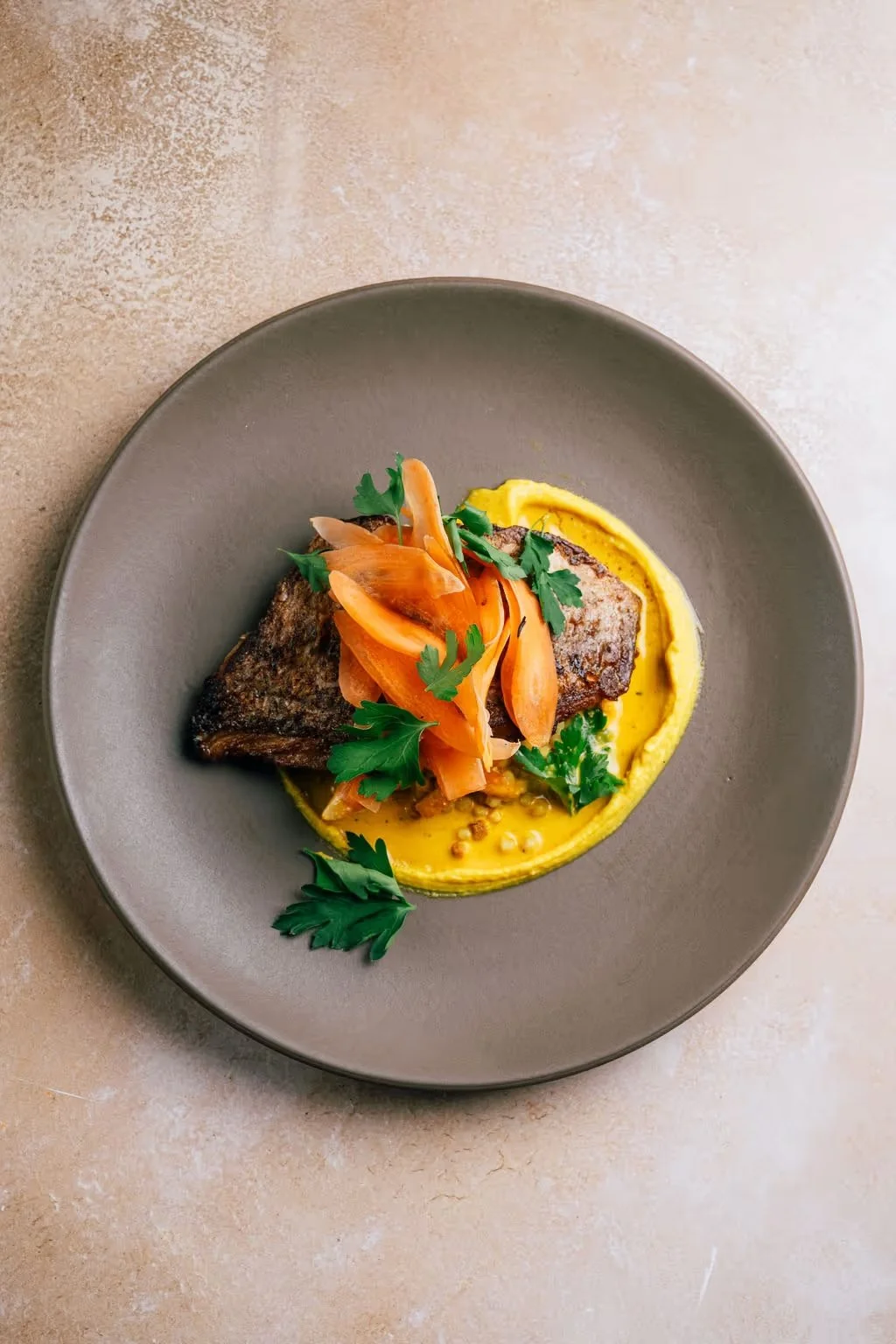 Pan-seared fish fillet garnished with carrots and cilantro, served over yellow sauce on a gray plate.