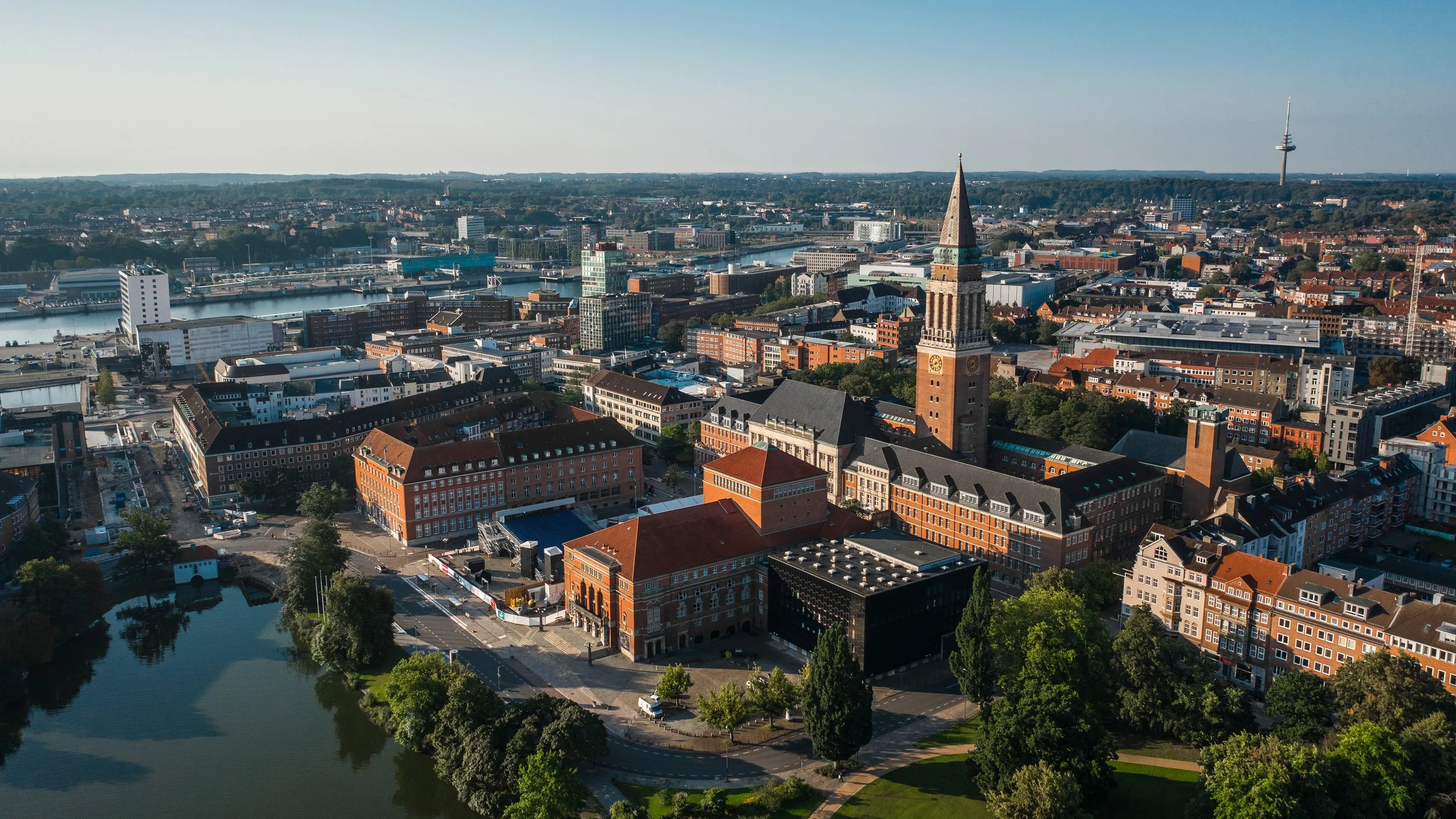 Luftaufnahme der Kieler Innenstadt mit dem Rathaus, historischen Backsteinbauten und der Förde im Hintergrund.