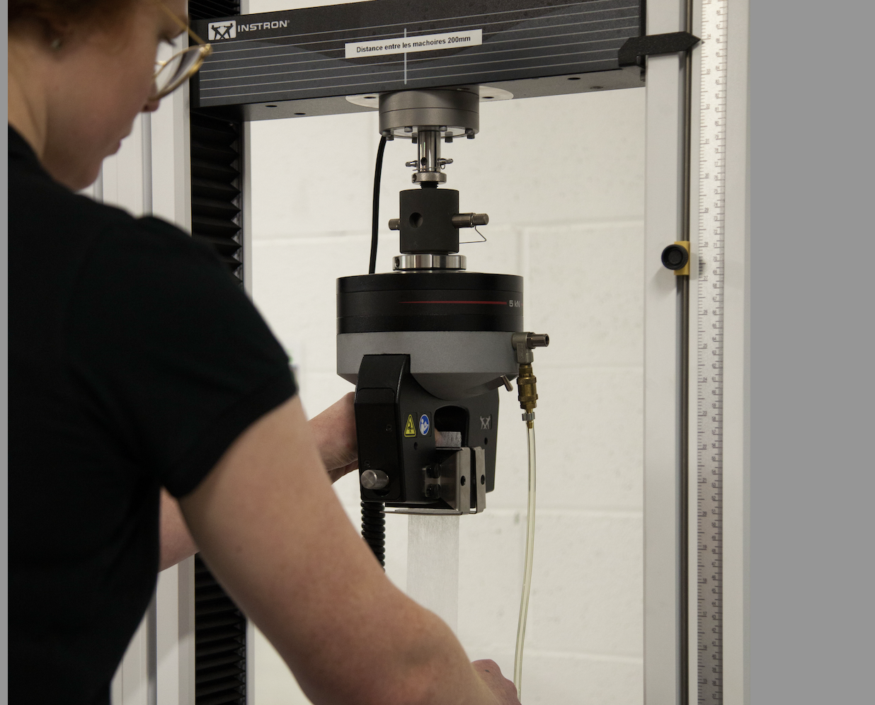 A person adjusting a mechanical testing machine in a laboratory setting.