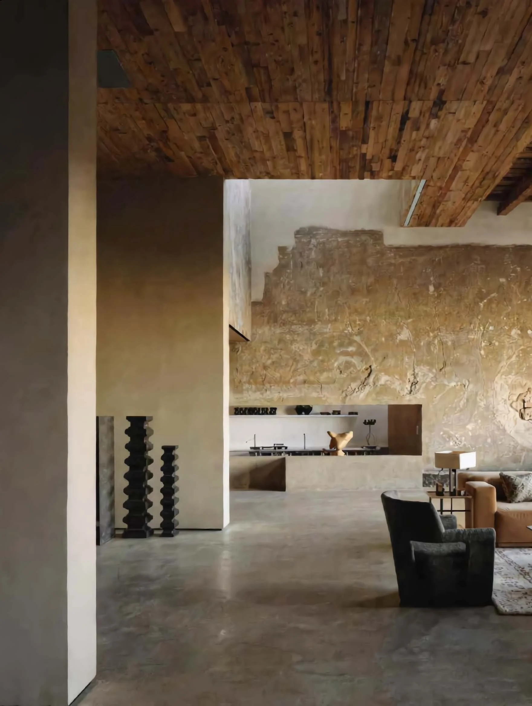 Interno di una casa con pareti in pietra, soffitto in legno, area living con divani e lampada.