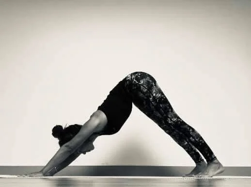 A woman practicing yoga in downward dog pose in a studio.